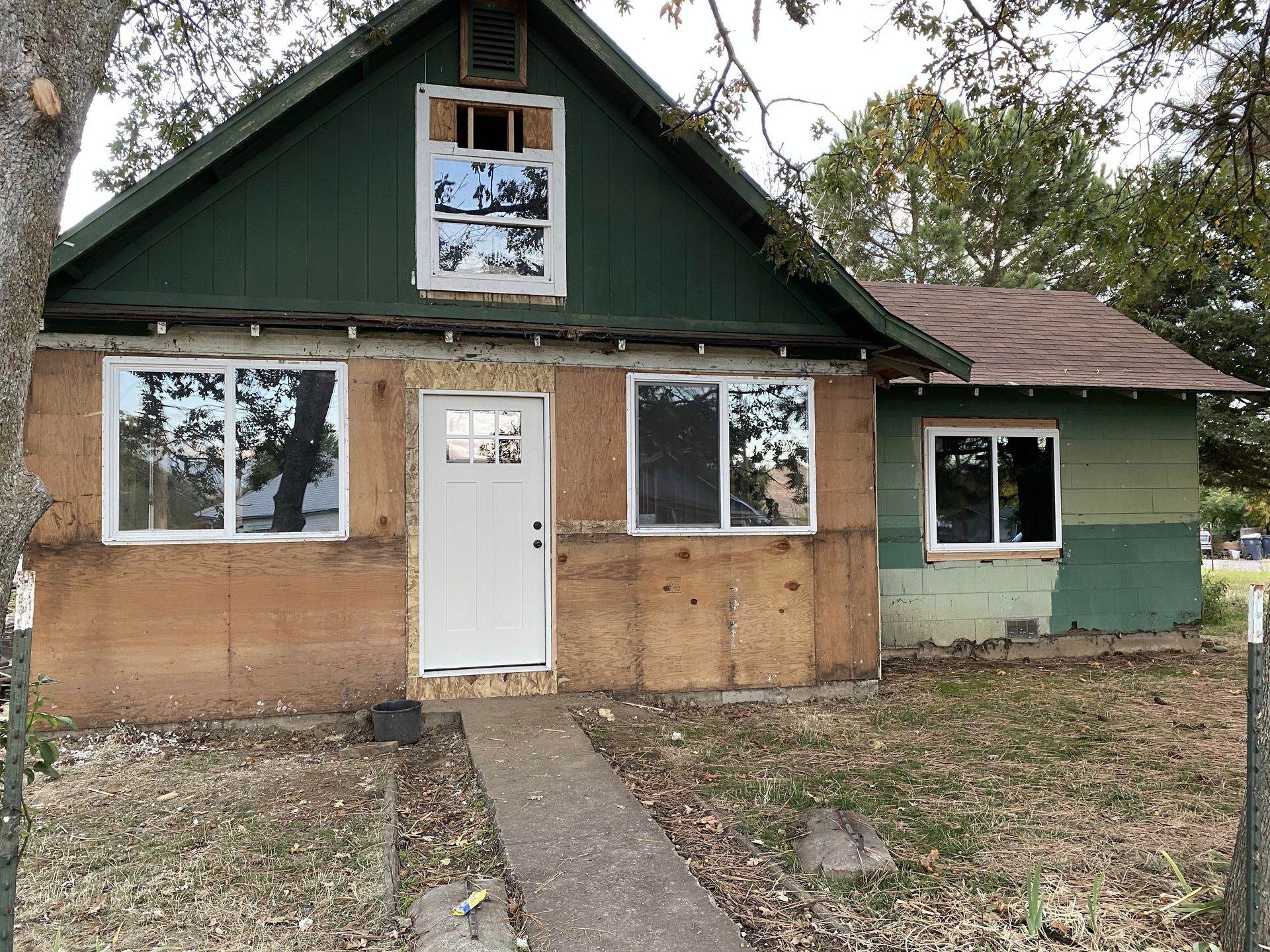 Small house with green gable, brown stucco walls, white windows, and a white door.