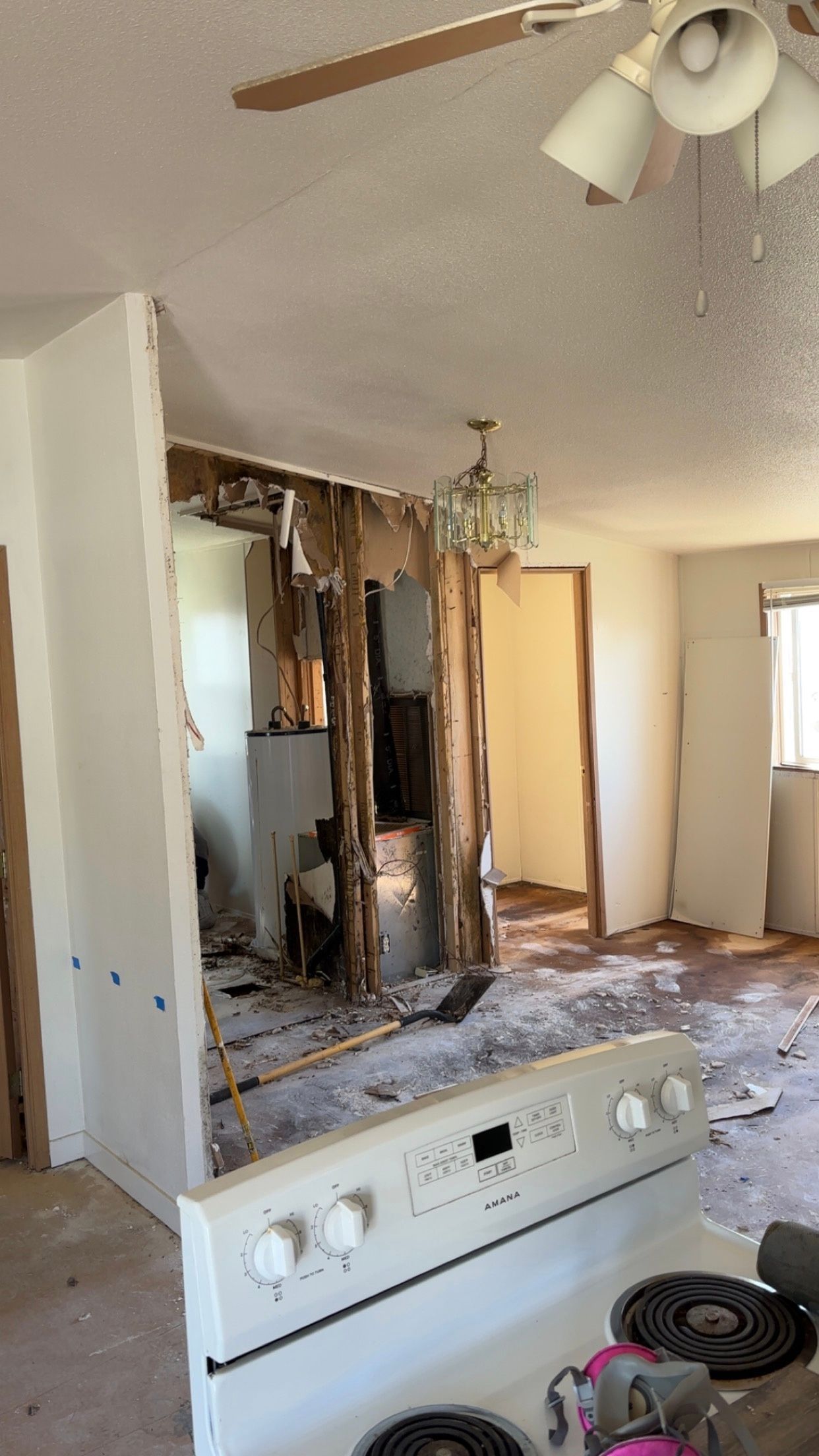 Interior view of a damaged kitchen and living area, with exposed walls, a stove, and a partially visible chandelier.