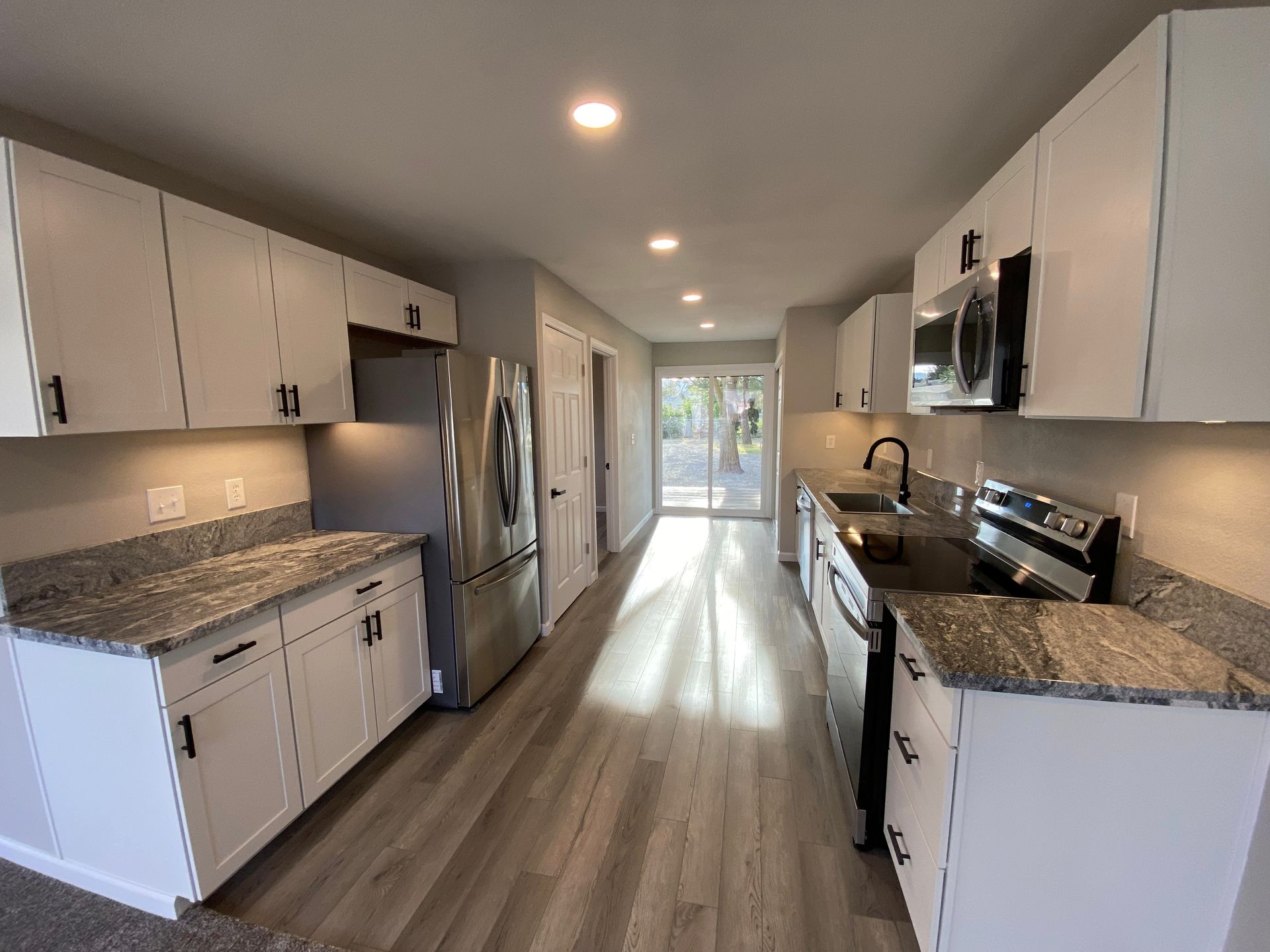 White kitchen with stainless steel appliances, gray countertops, and wood flooring.