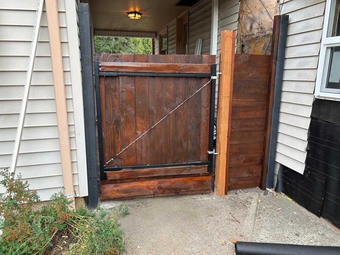 Wooden gate in a doorway, brown planks, black metal frame, light gray concrete path, outside.