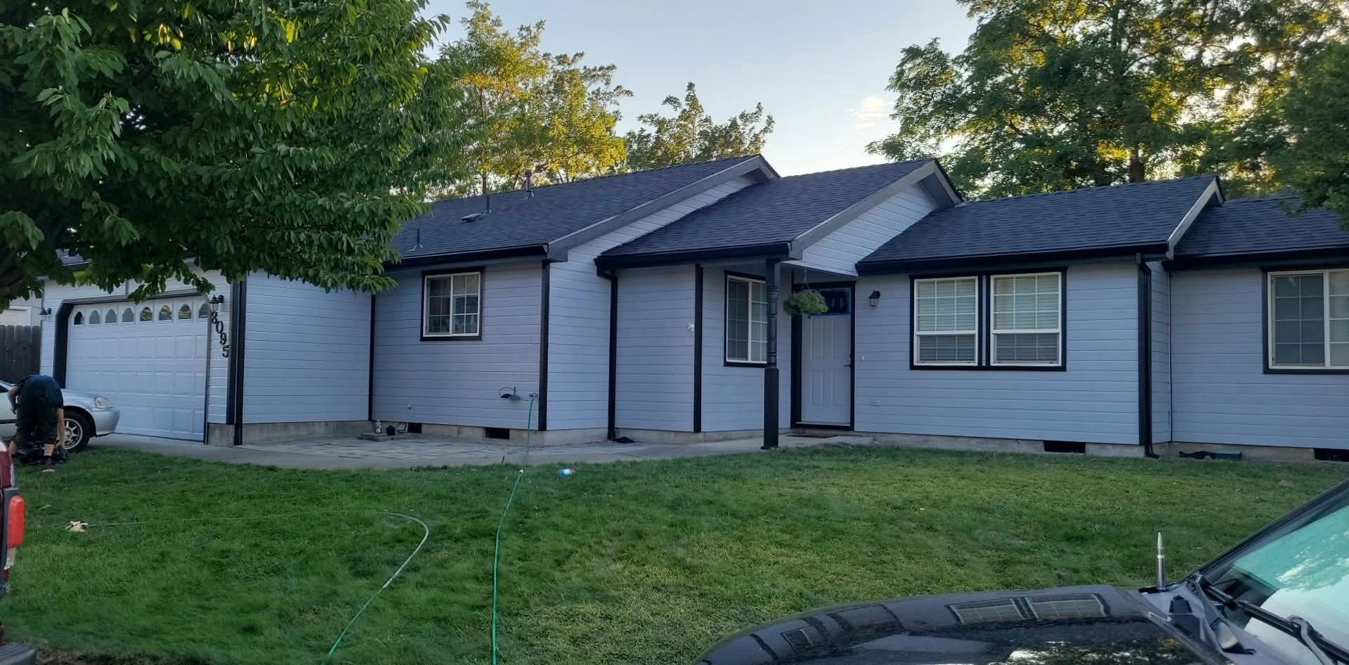 Gray house with black trim and roof, green lawn, trees.