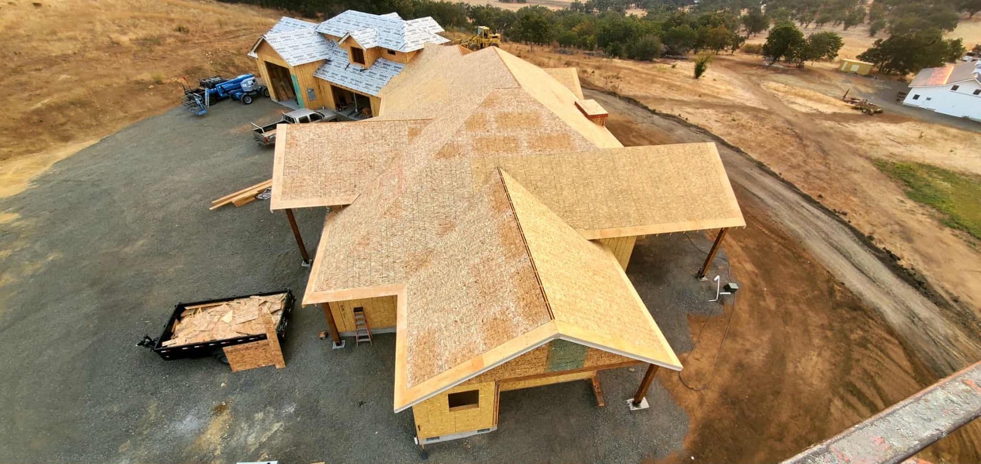 Aerial view of a house under construction with exposed wooden framing and plywood roofing.