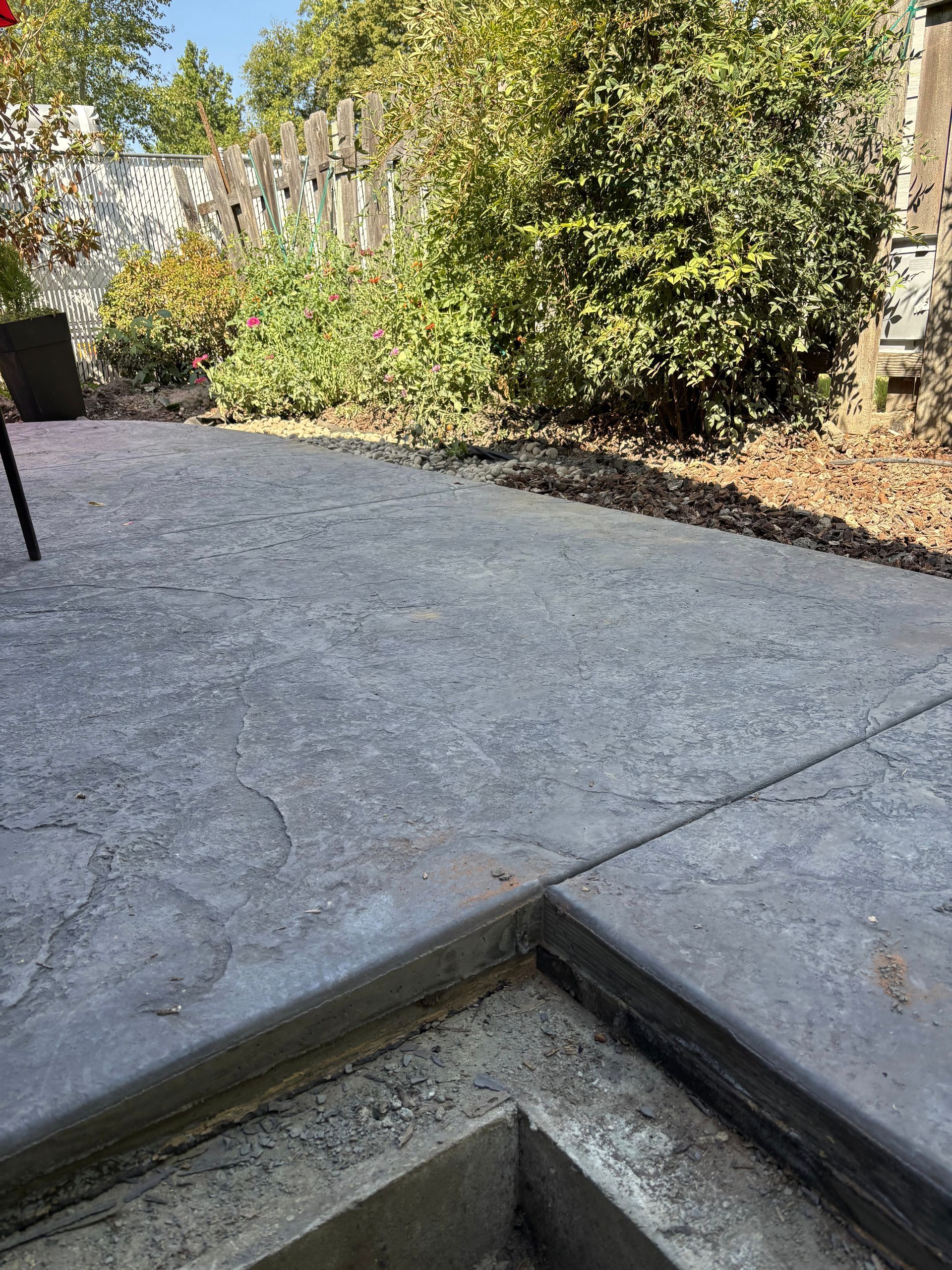 Concrete patio with a dark edge and a garden in the background.