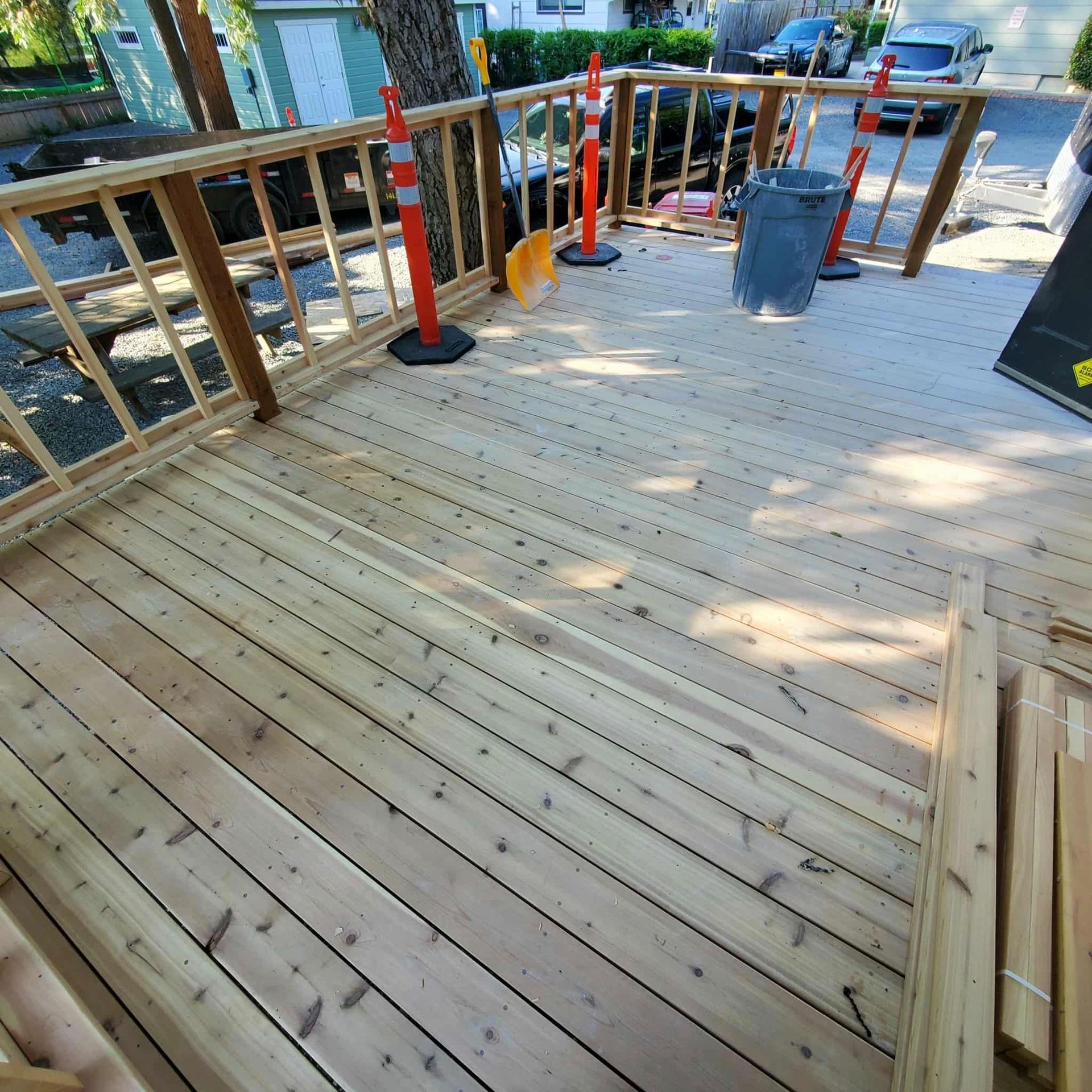 Newly built wooden deck with railing, orange construction cones, and a trash can.