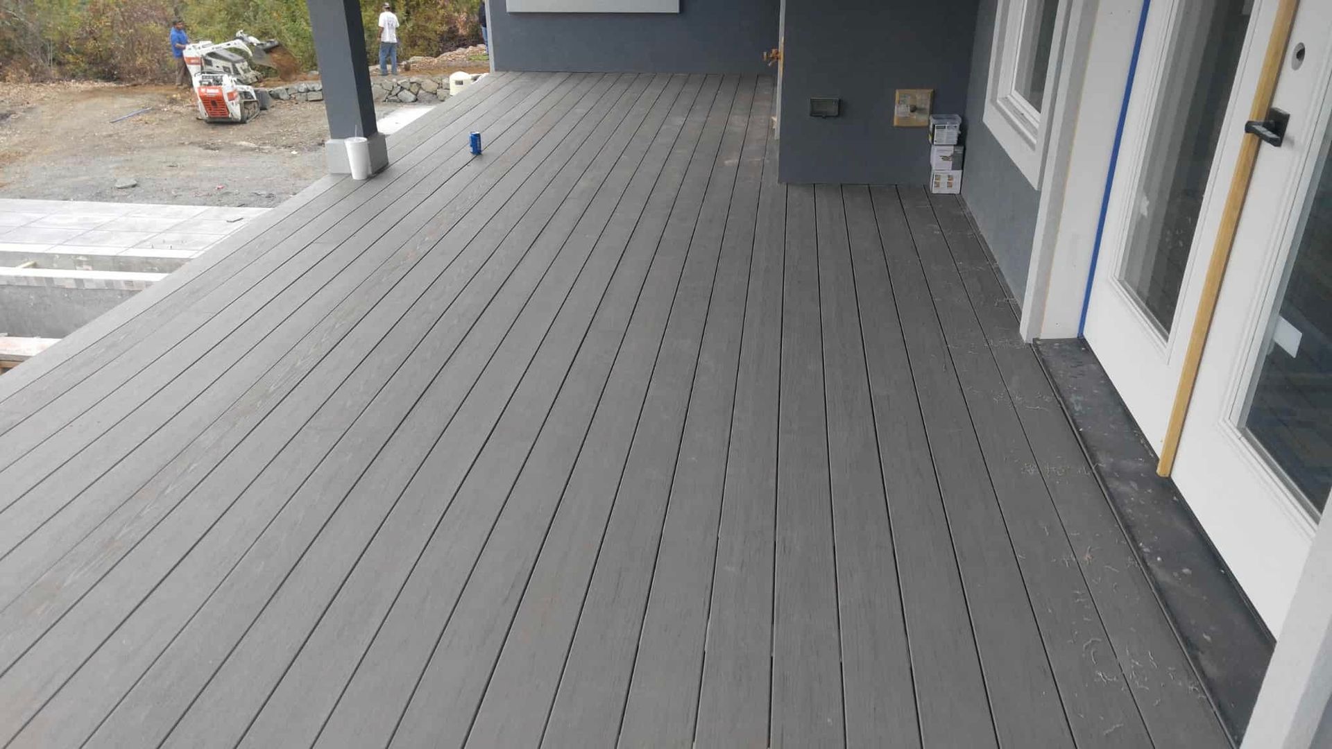 Gray composite deck extends from a building, next to a white door. Construction site in background.