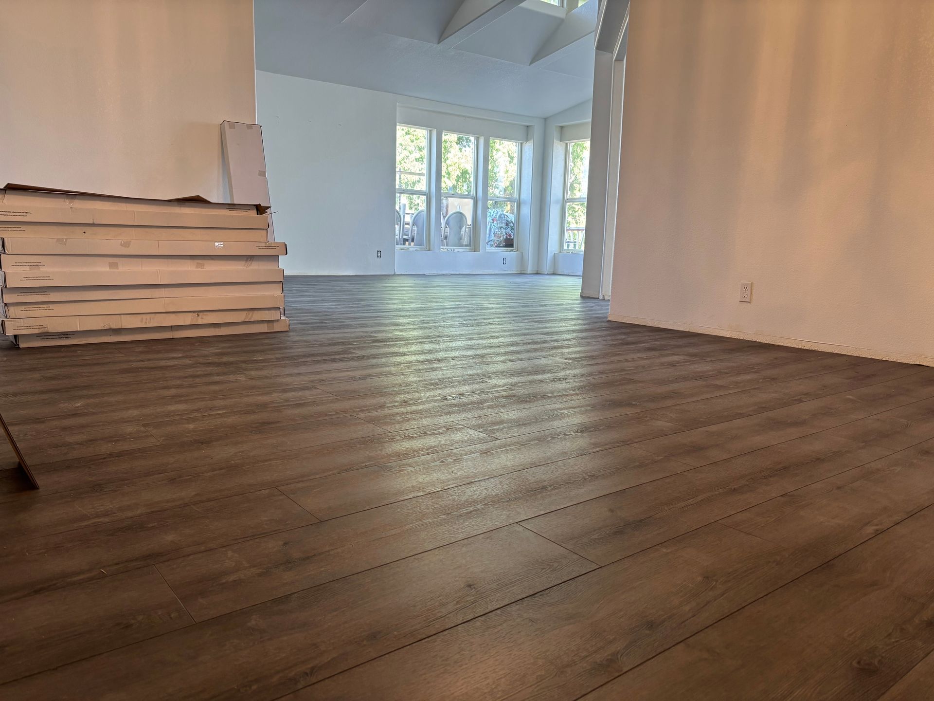 Newly installed brown wood-look flooring in a mostly white room with a pile of wood planks.