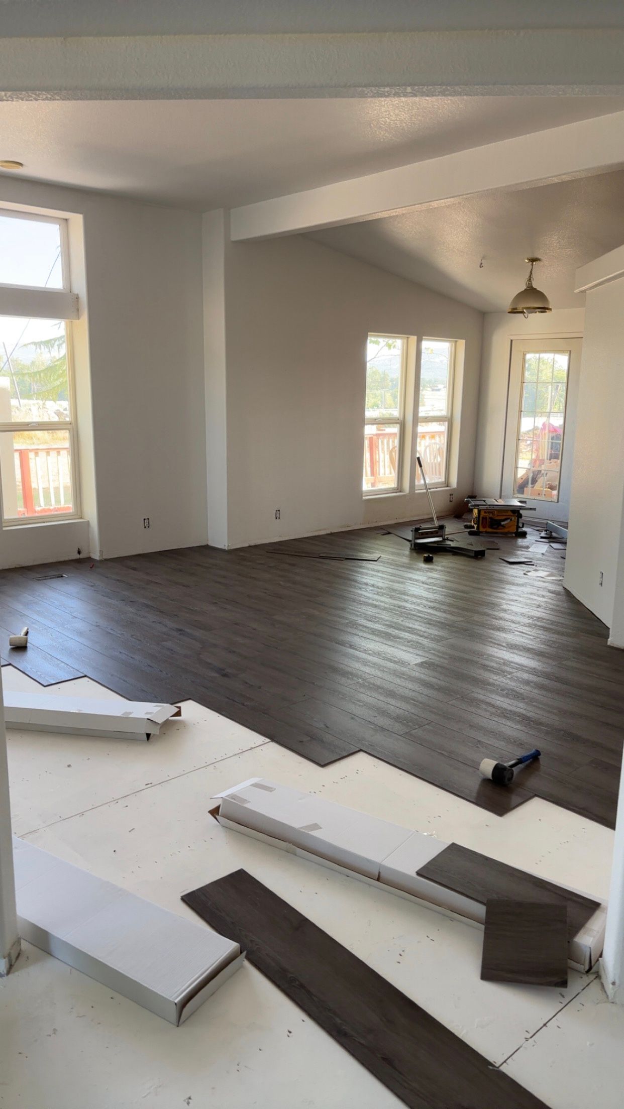 Room with dark wood-look flooring being installed; white walls, windows, and ceiling beams.