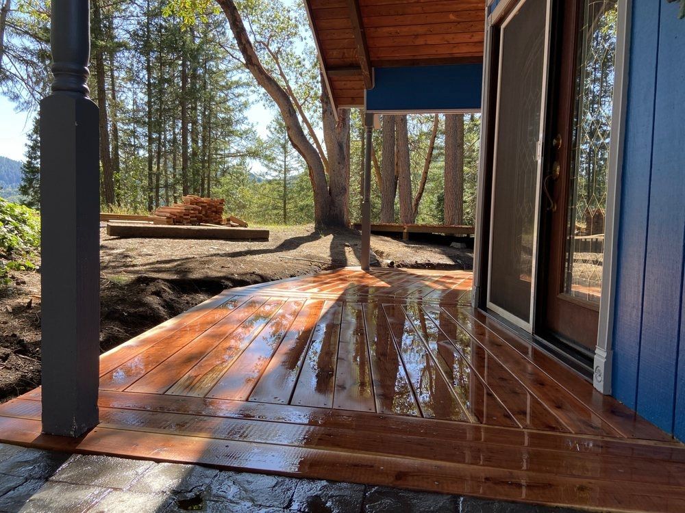 Wooden deck with wet, glossy finish. Blue house exterior, surrounded by trees, sunny day.