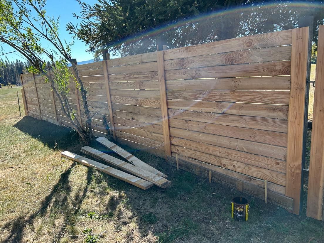 Wooden fence in a grassy field, partially constructed with planks and posts, under a bright sky.