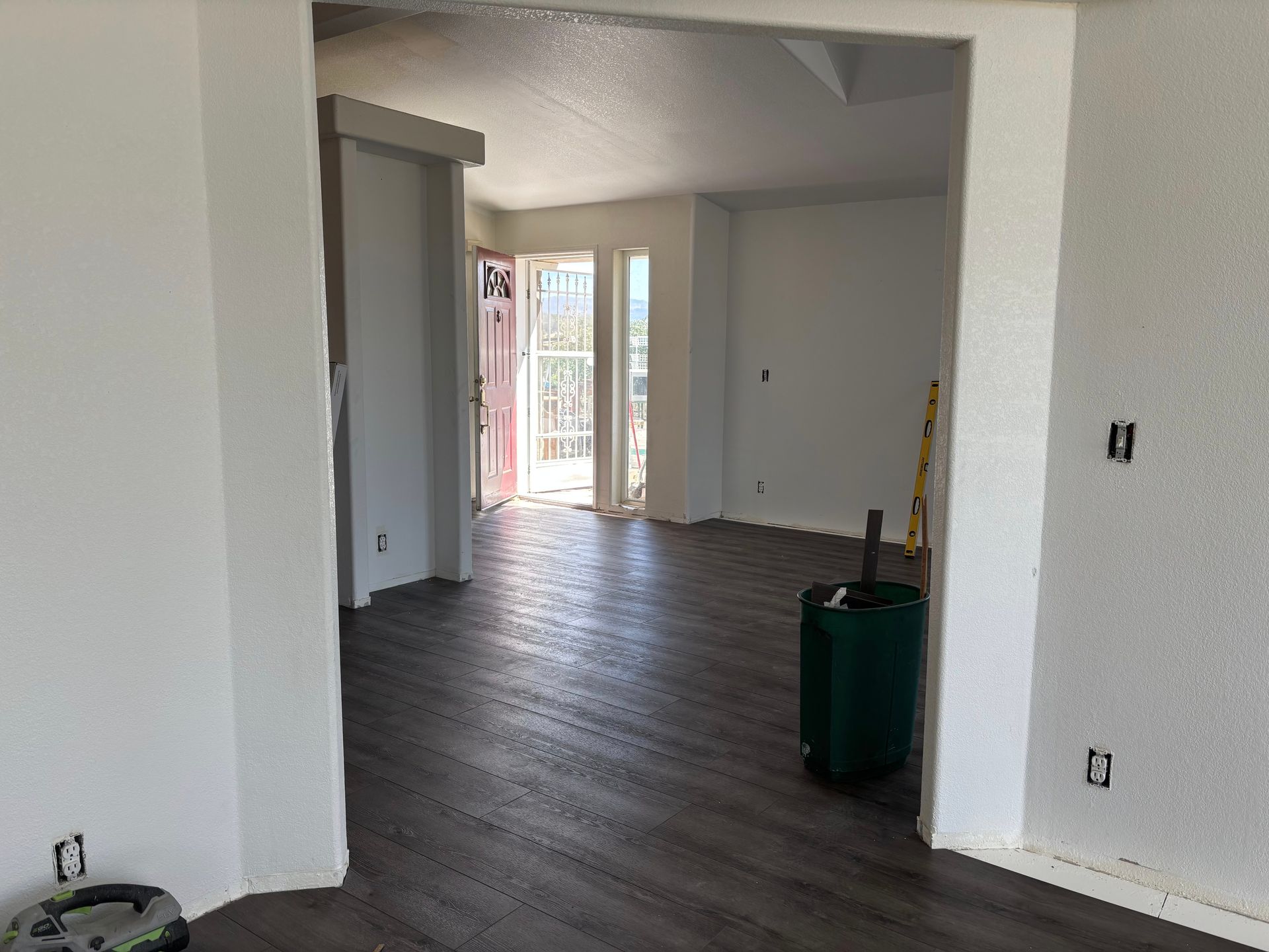 An empty room with dark wood-look floors, white walls, and an open doorway to a balcony.