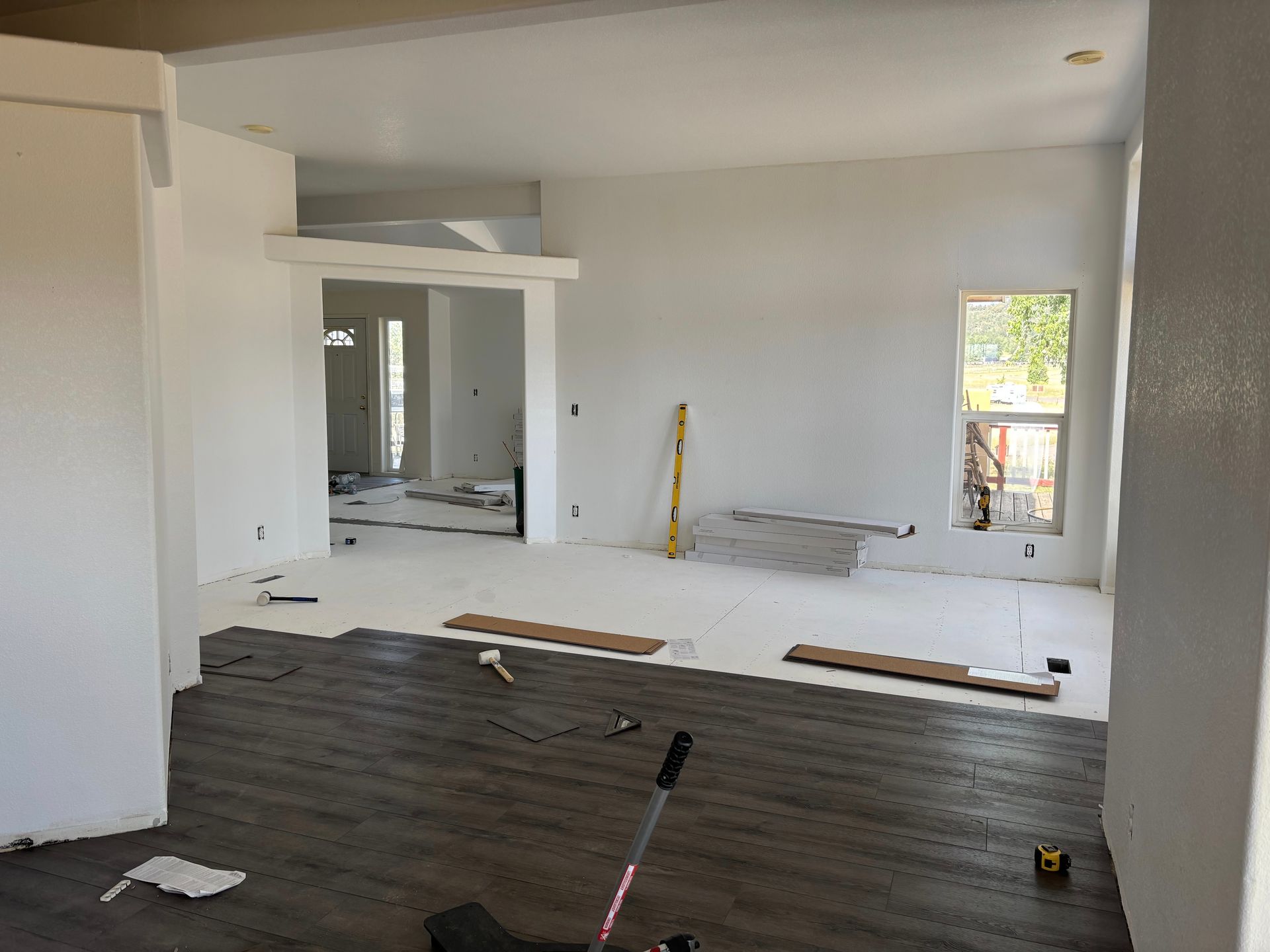 Interior view of a house under construction. Dark wood-look flooring installed, walls painted white, open doorways.