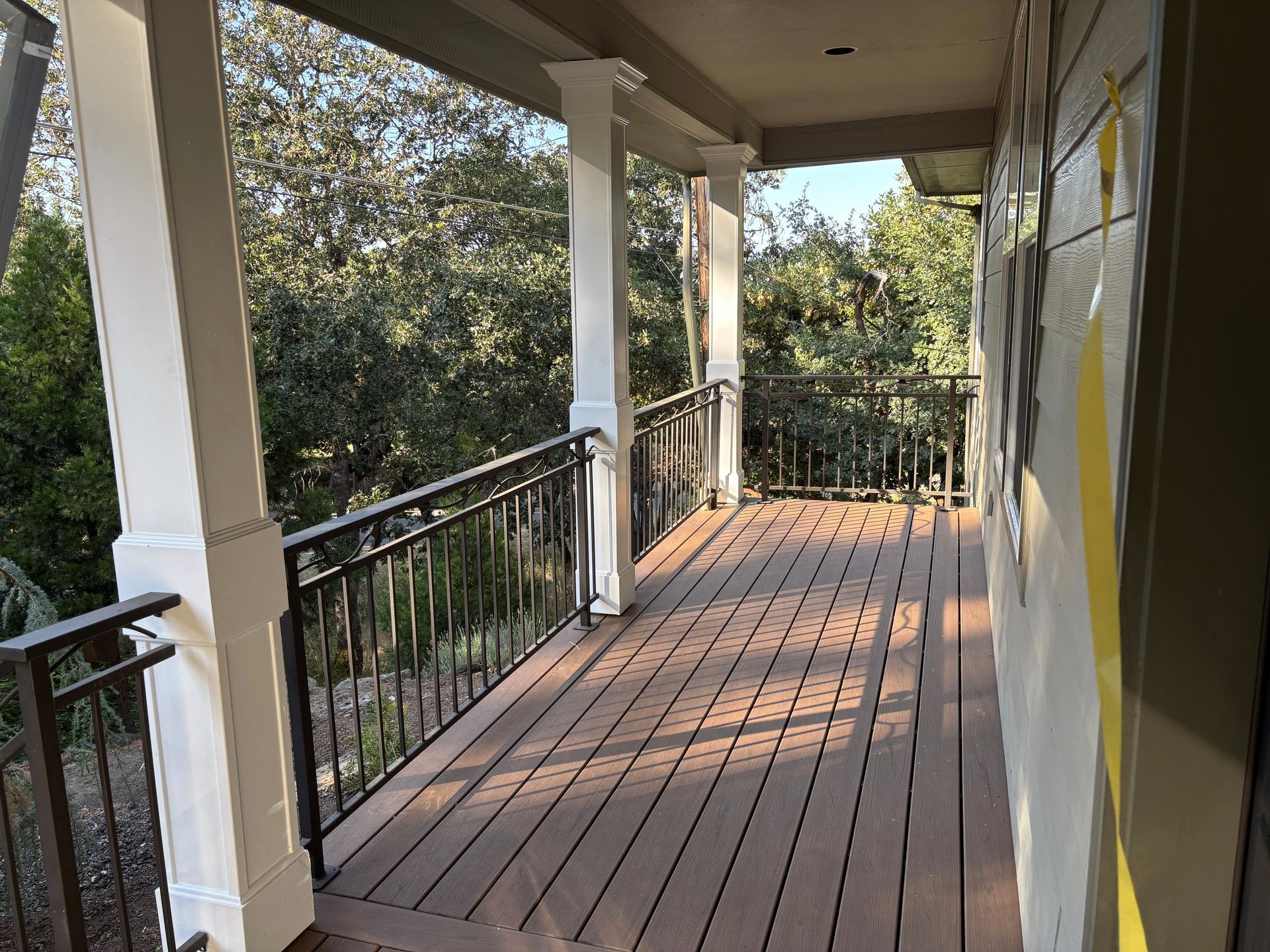 Covered wooden porch with black railing, white columns, and a view of trees.