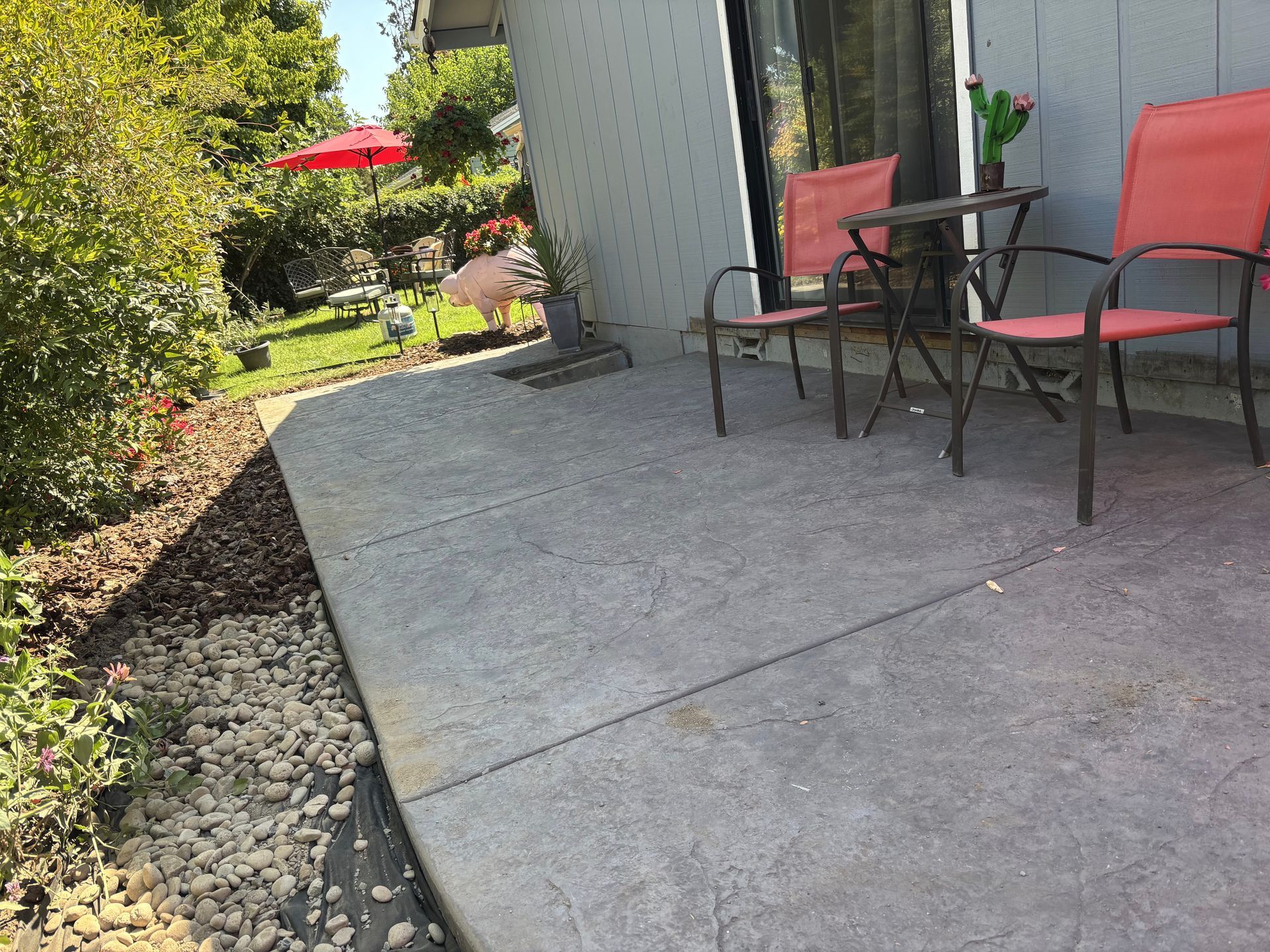 Concrete patio with red chairs and table, a yard with a flamingo and red umbrella in the background.