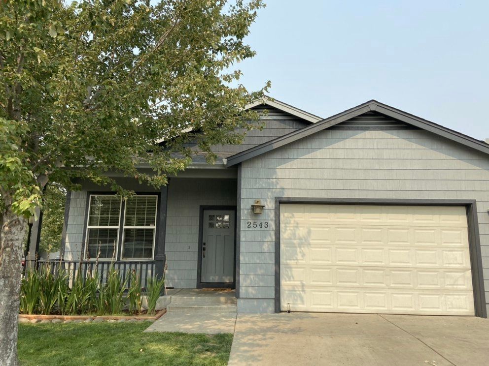 Gray house with a white garage door and a tree in front.