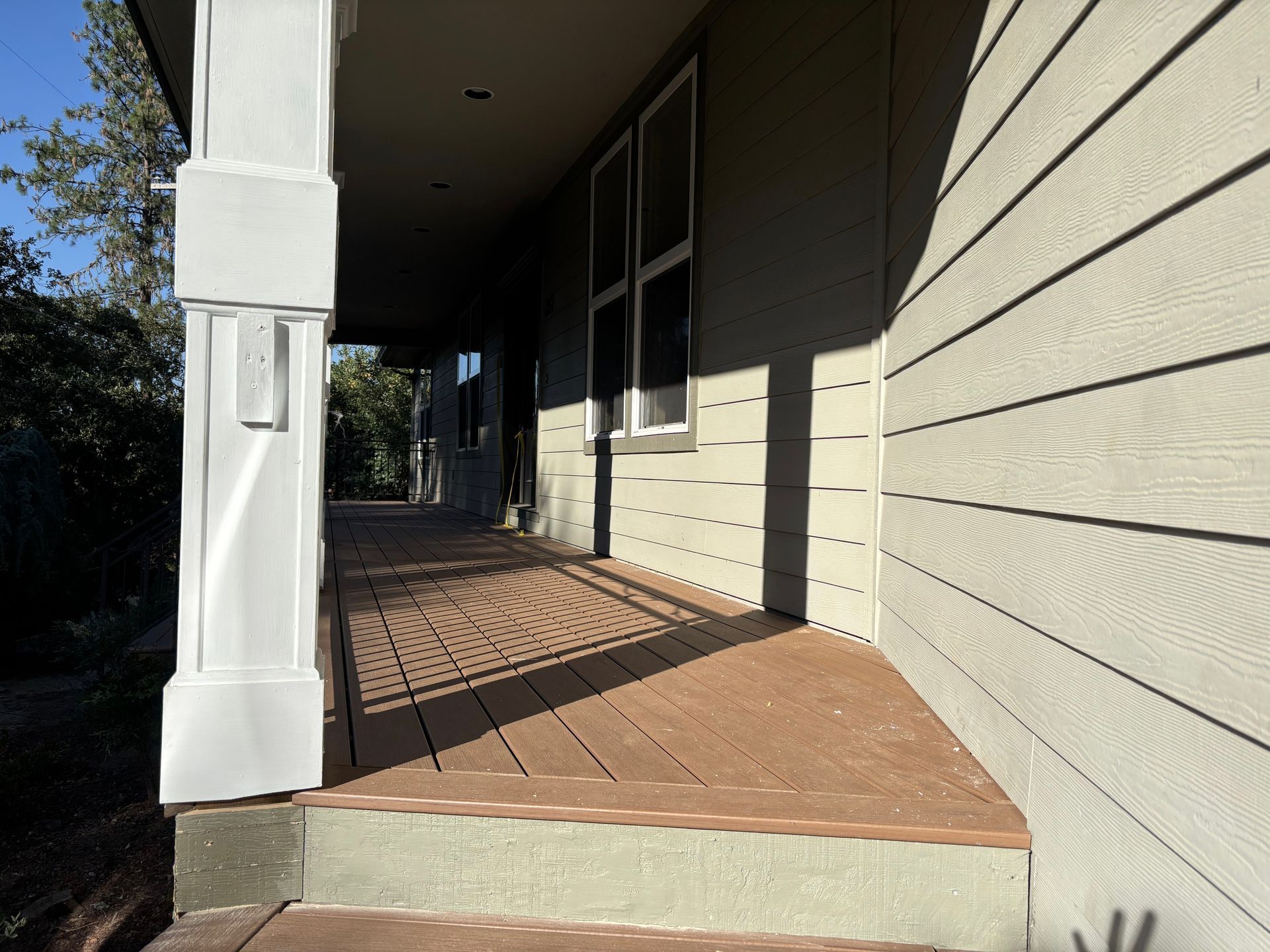 Covered porch with brown composite decking, white pillar, and light green siding.