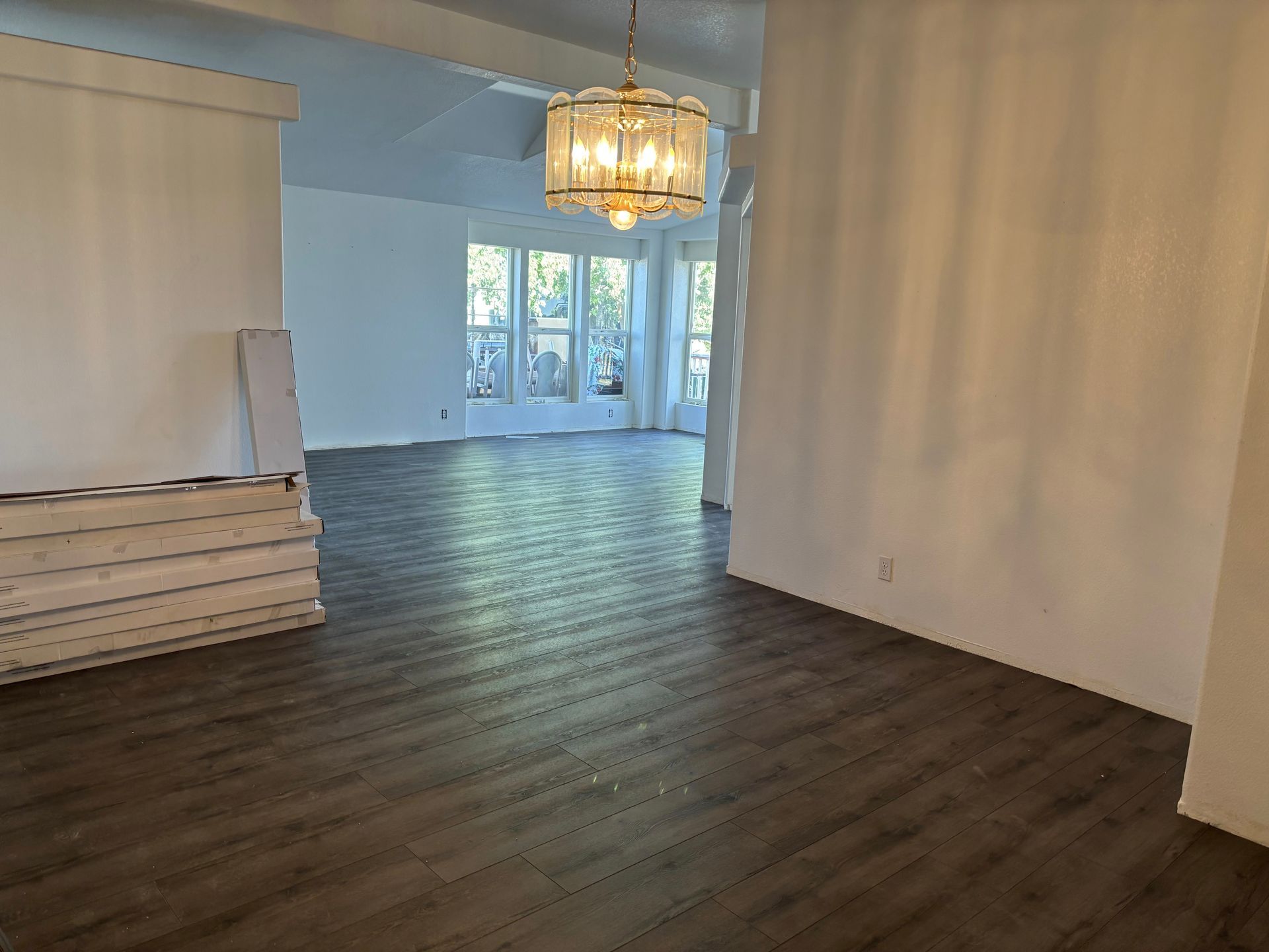 Open-concept living space with dark wood floors, white walls, and a crystal chandelier.