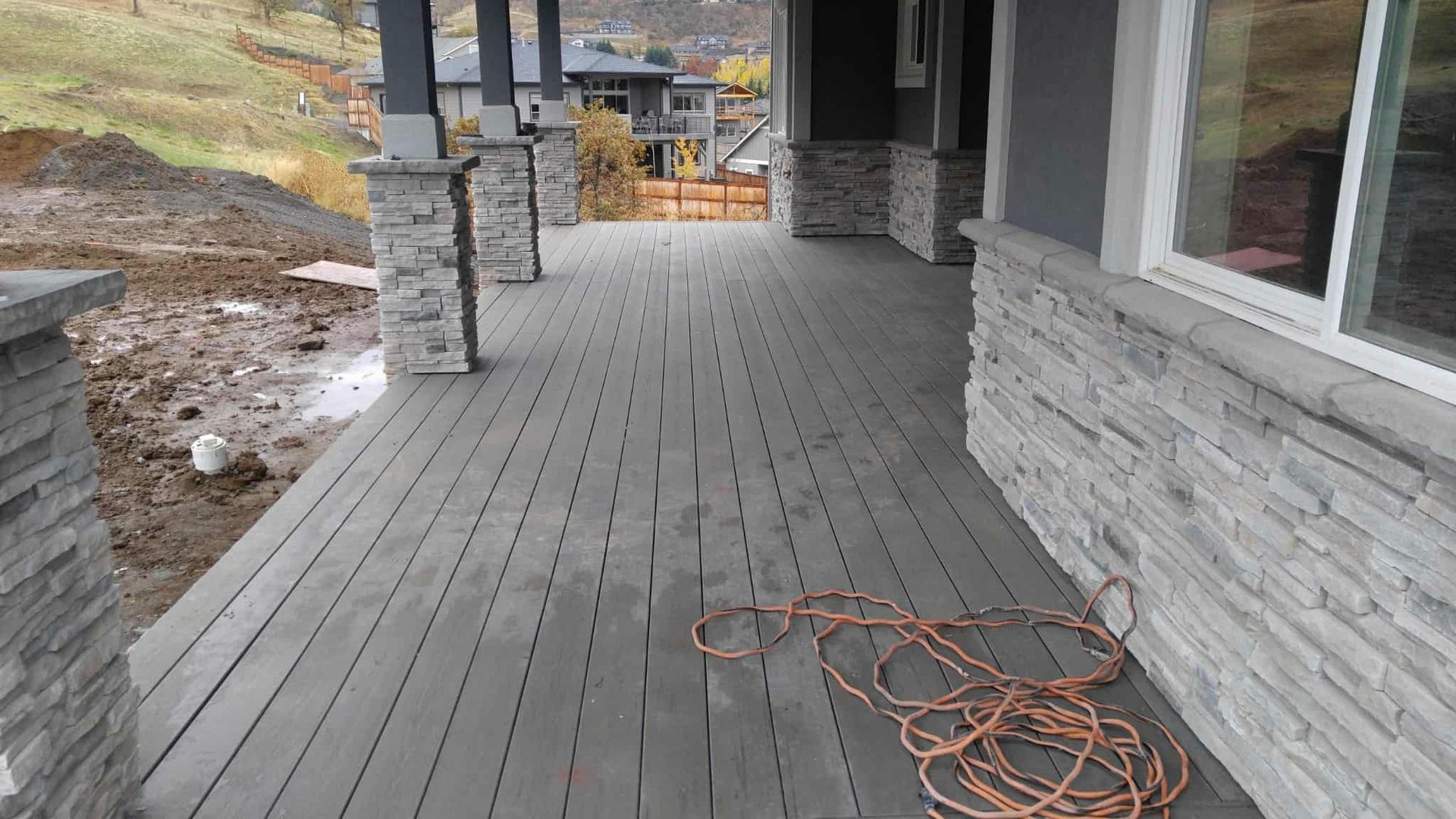 Gray wooden porch with stacked stone columns, coiled orange rope on the floor, new construction.