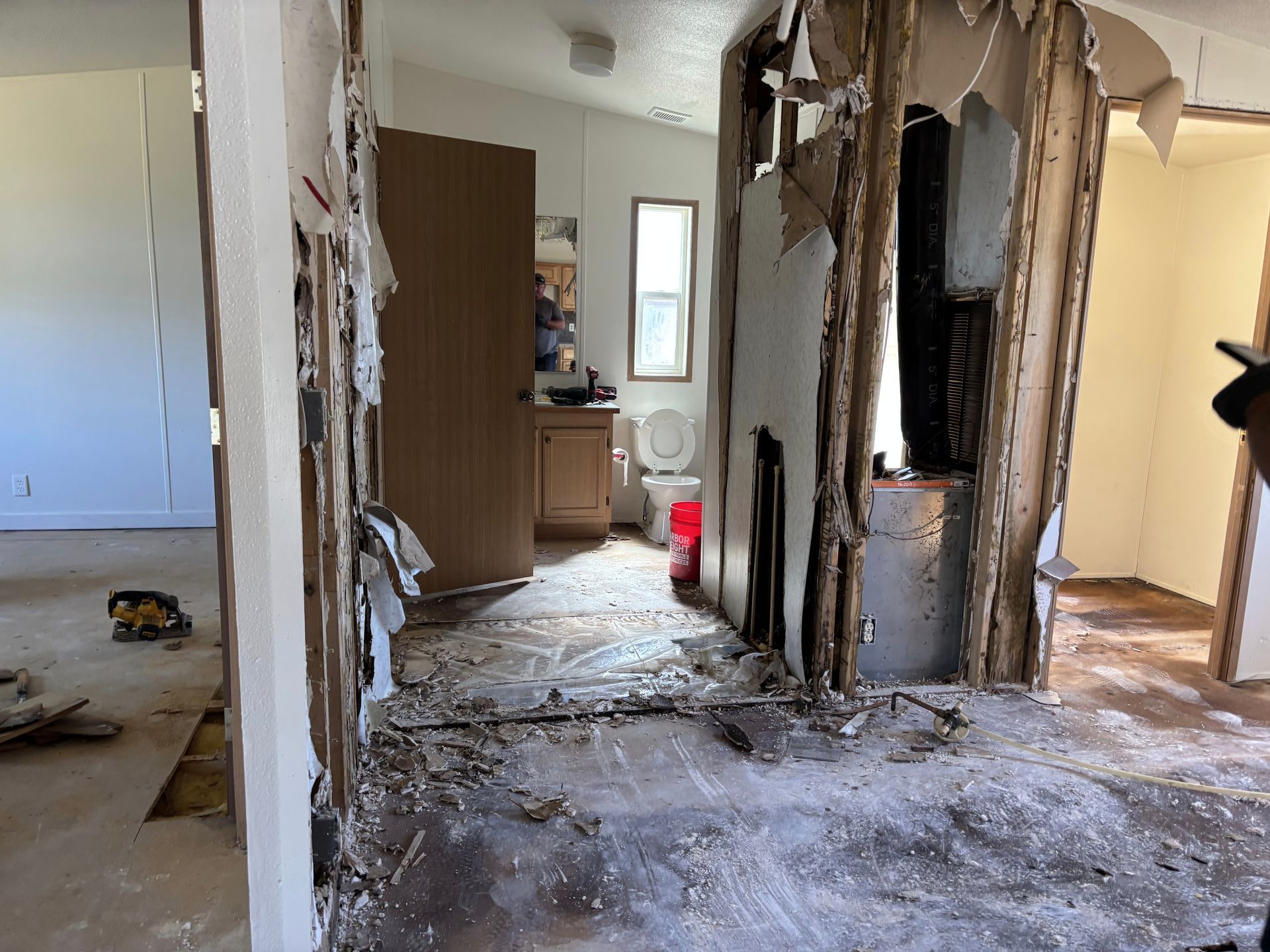 Interior of a home in disrepair, walls torn open, debris on the floor. Doorways lead to other rooms.