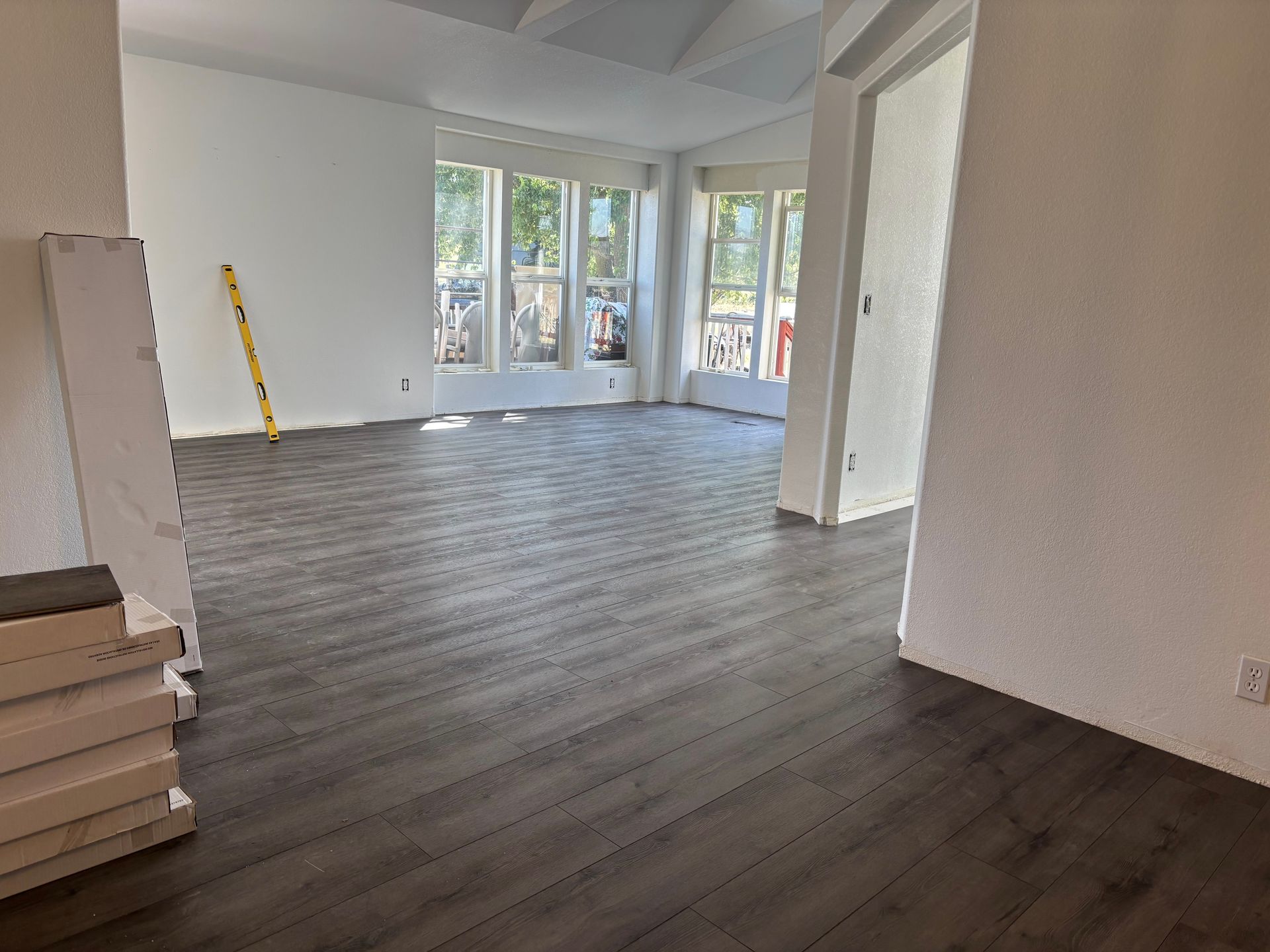 Dark wood-look flooring in a room with white walls, a windowed wall, and an open doorway.