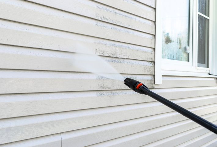 A person is using a high pressure washer to clean the side of a house.