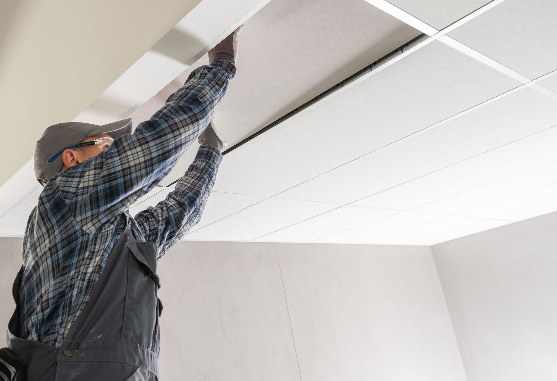 A man is hanging a tile ceiling in a room.