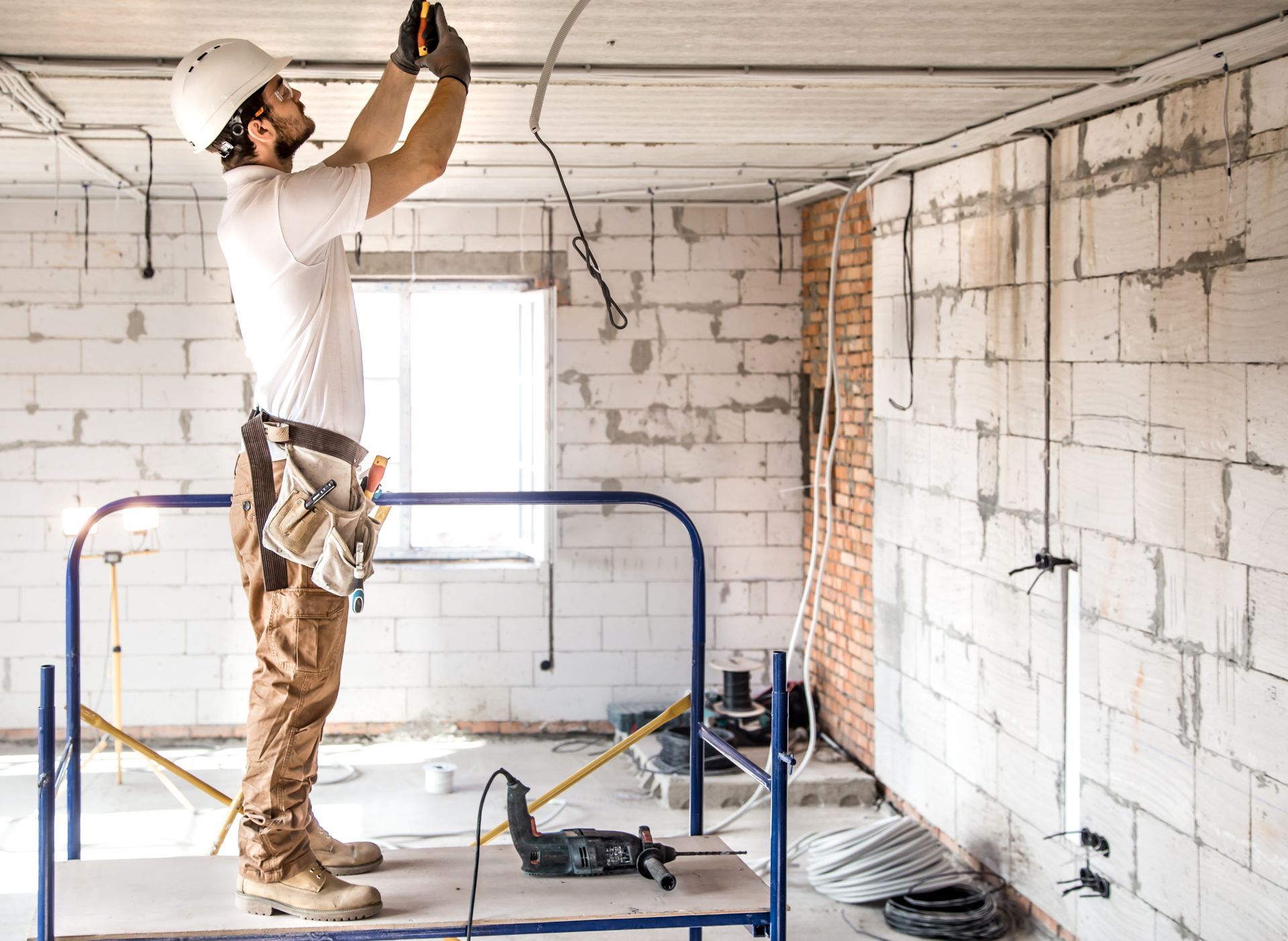A man is kneeling on the floor using a drill on a piece of wood.