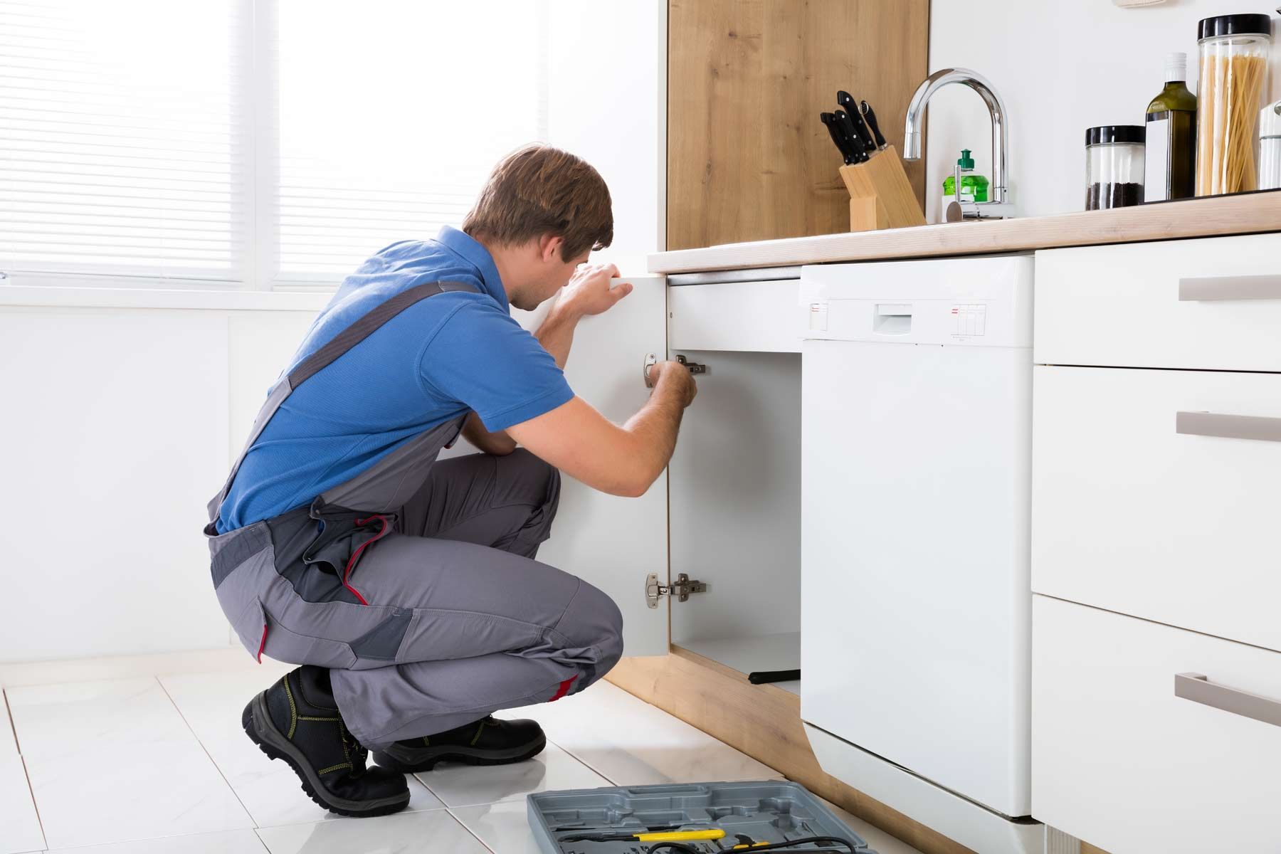 A plumber is fixing a sink in a kitchen.