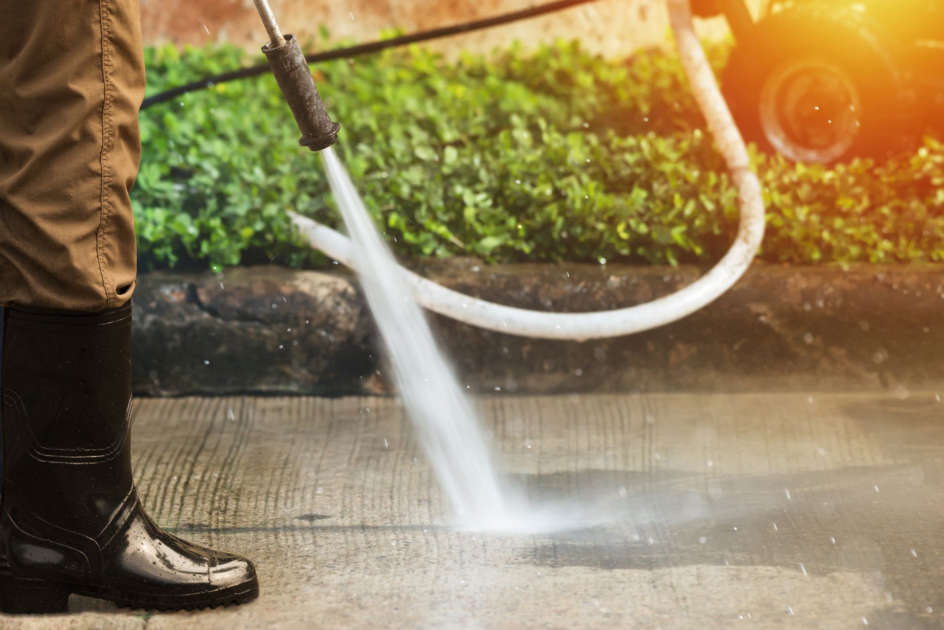 A person is using a high pressure washer to clean a sidewalk.