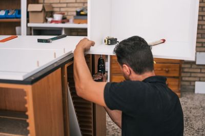 A man is using a drill to assemble a cabinet.
