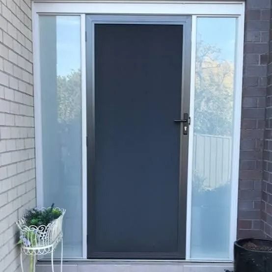 A Black Door with A Screen and A White Frame Is on The Side of A Brick Building — Southside Aluminium Windows and Doors in Yallah, NSW