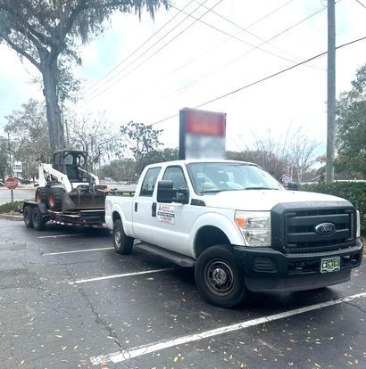 a white truck is parked next to a trailer with a bulldozer on it .
