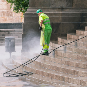 Worker in neon safety gear pressure-washing stone steps amid mist and hoses