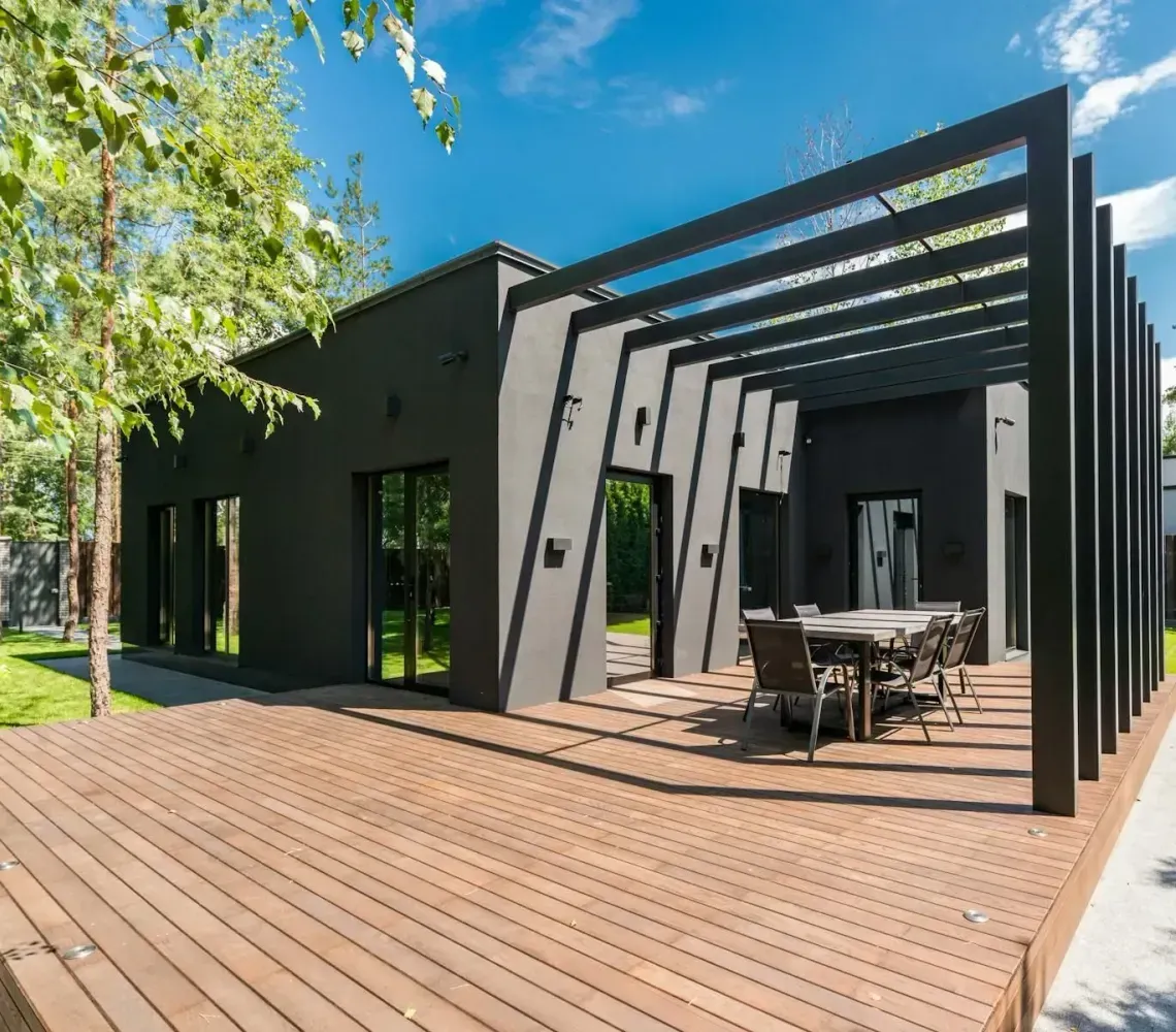 Modern black patio pavilion with wooden deck and outdoor dining table in a sunny garden