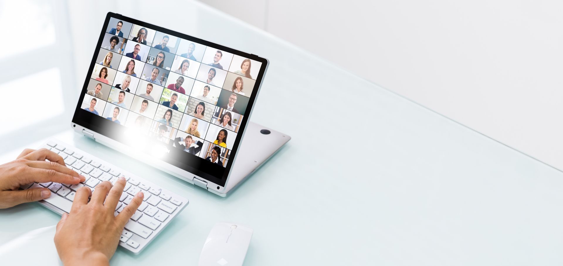 a person is typing on a laptop computer with a group of people on the screen .