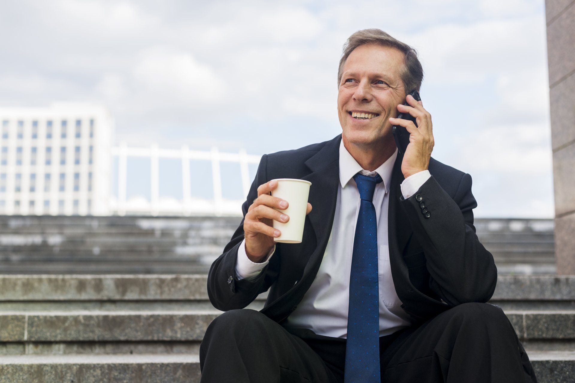 a man sitting on a staircase, using Iristel's business VoIP phone solutions and holding a cup of coffee