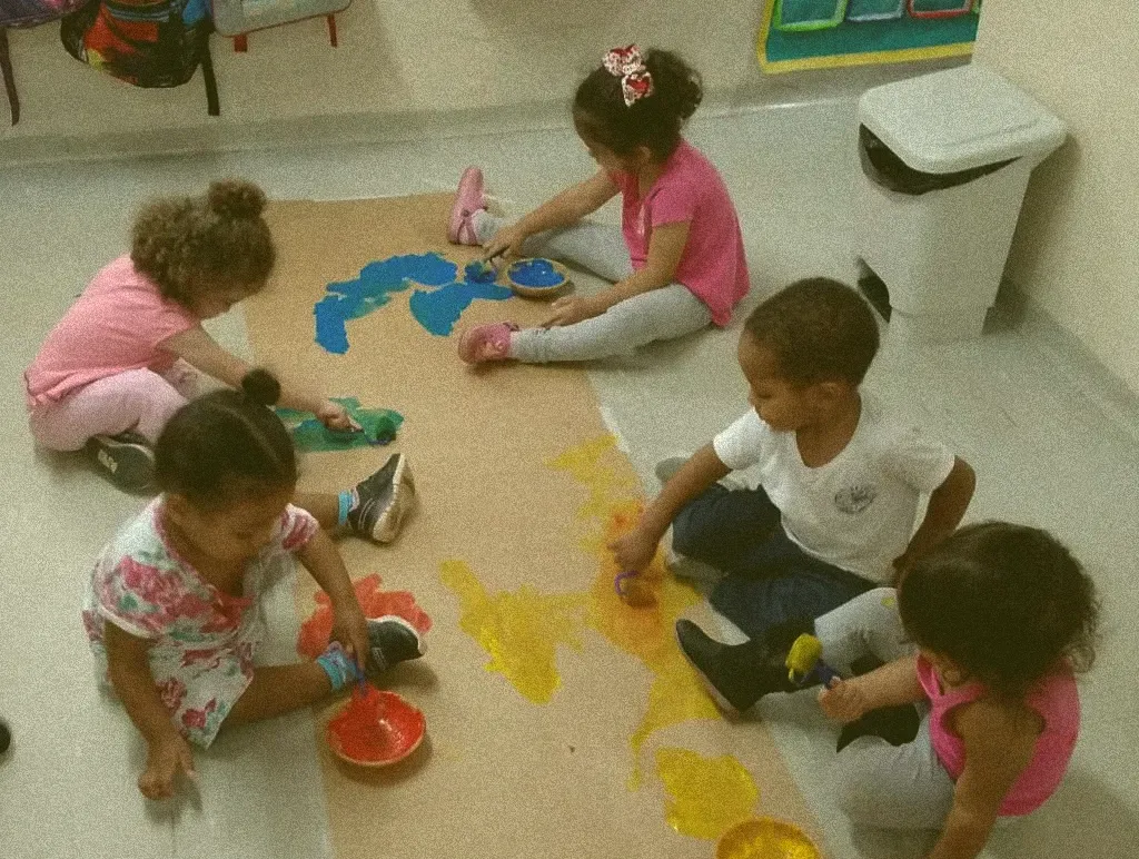 Um grupo de crianças está sentado no chão brincando com tinta