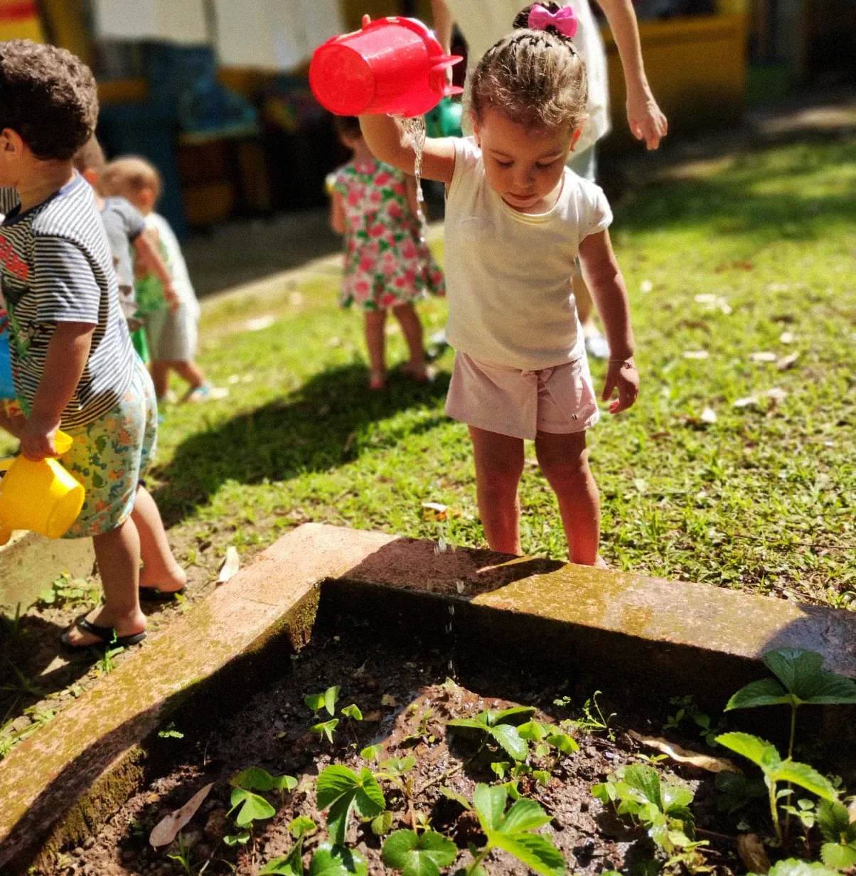 Uma menina está regando plantas com um regador vermelho