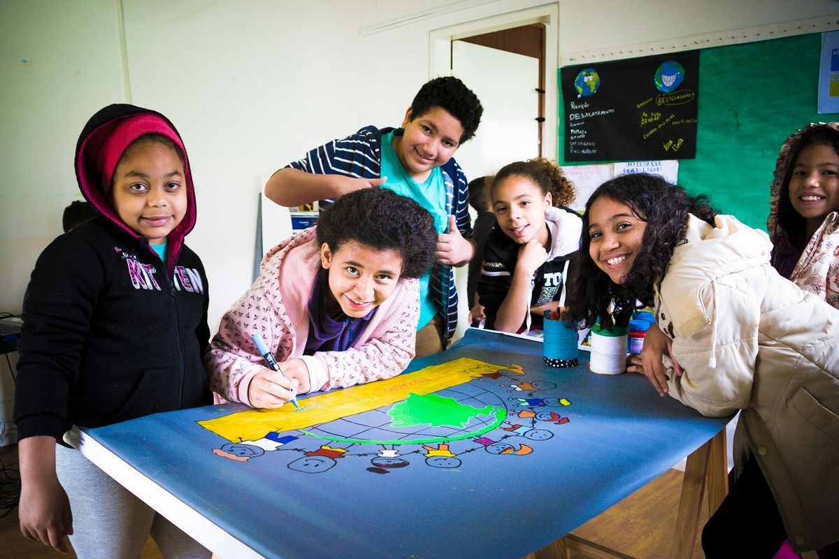 Um grupo de crianças está sentado ao redor de uma mesa com um mapa sobre ela.