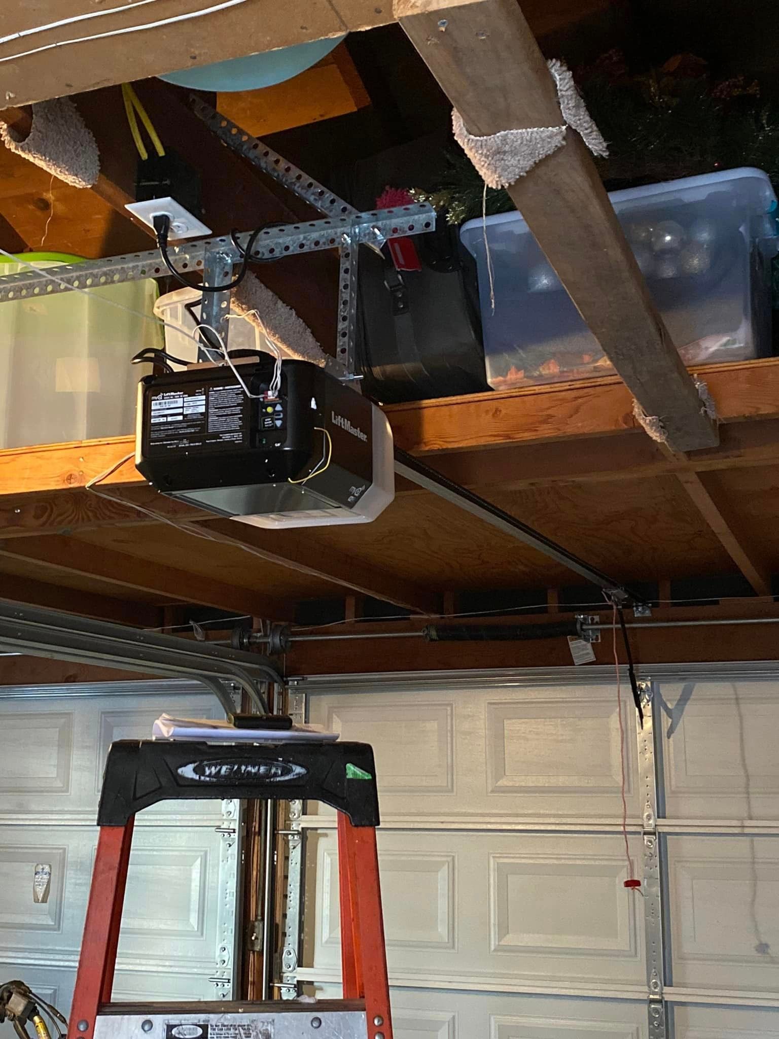 A red ladder is sitting under a garage door motor.