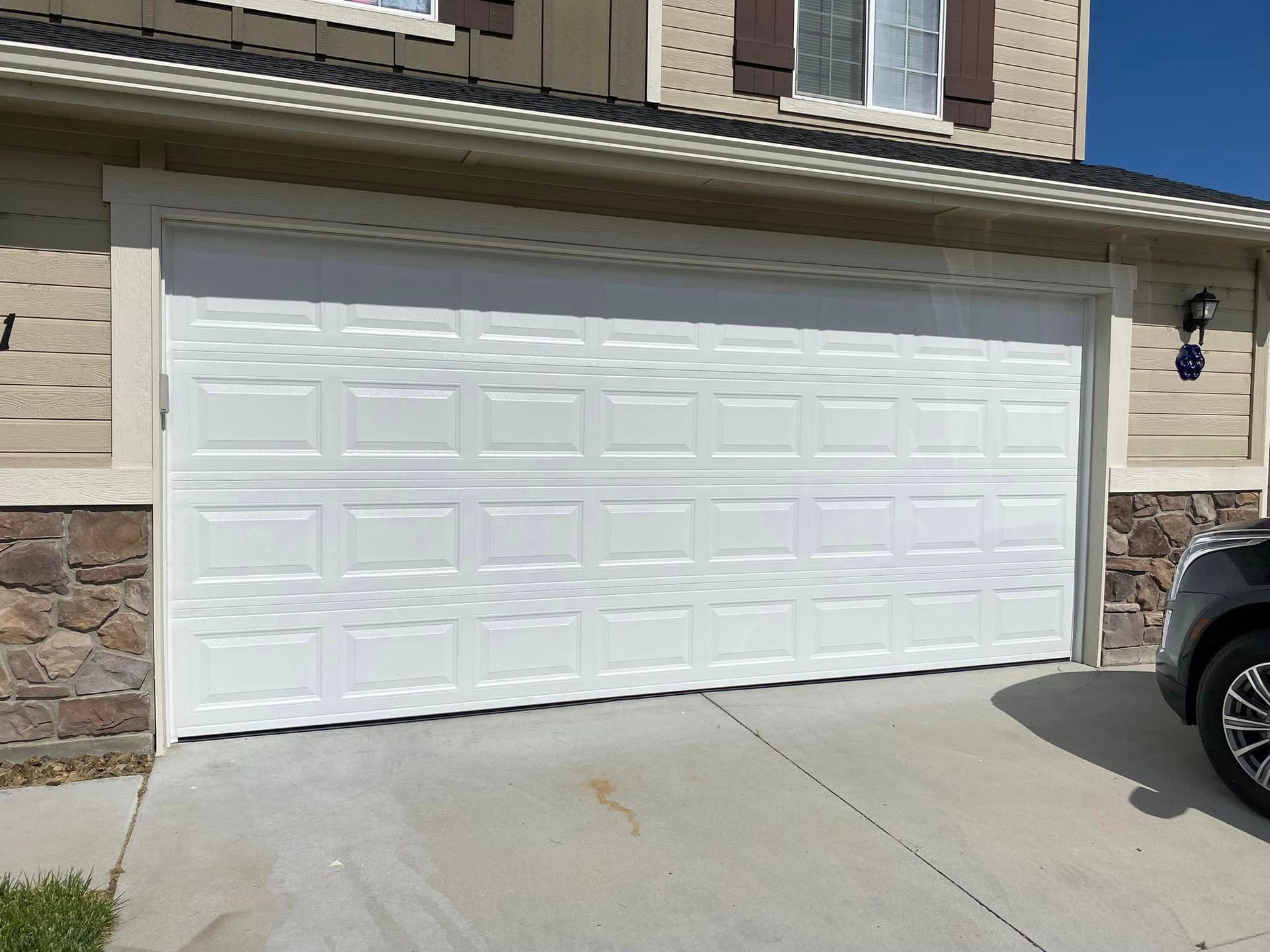 A white garage door is open and a car is parked in front of it.