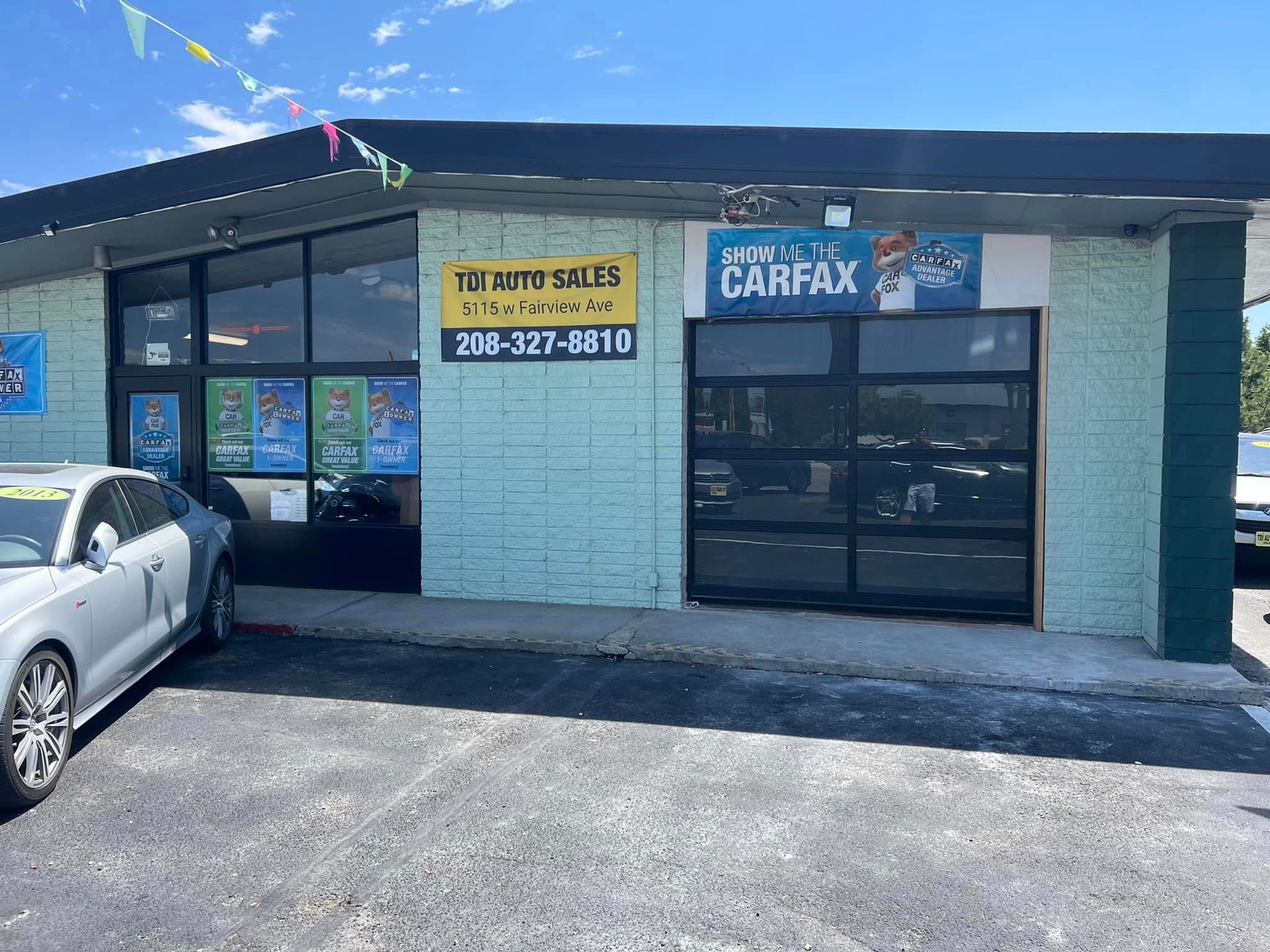 A car is parked in front of a car dealership that has new garage doors.