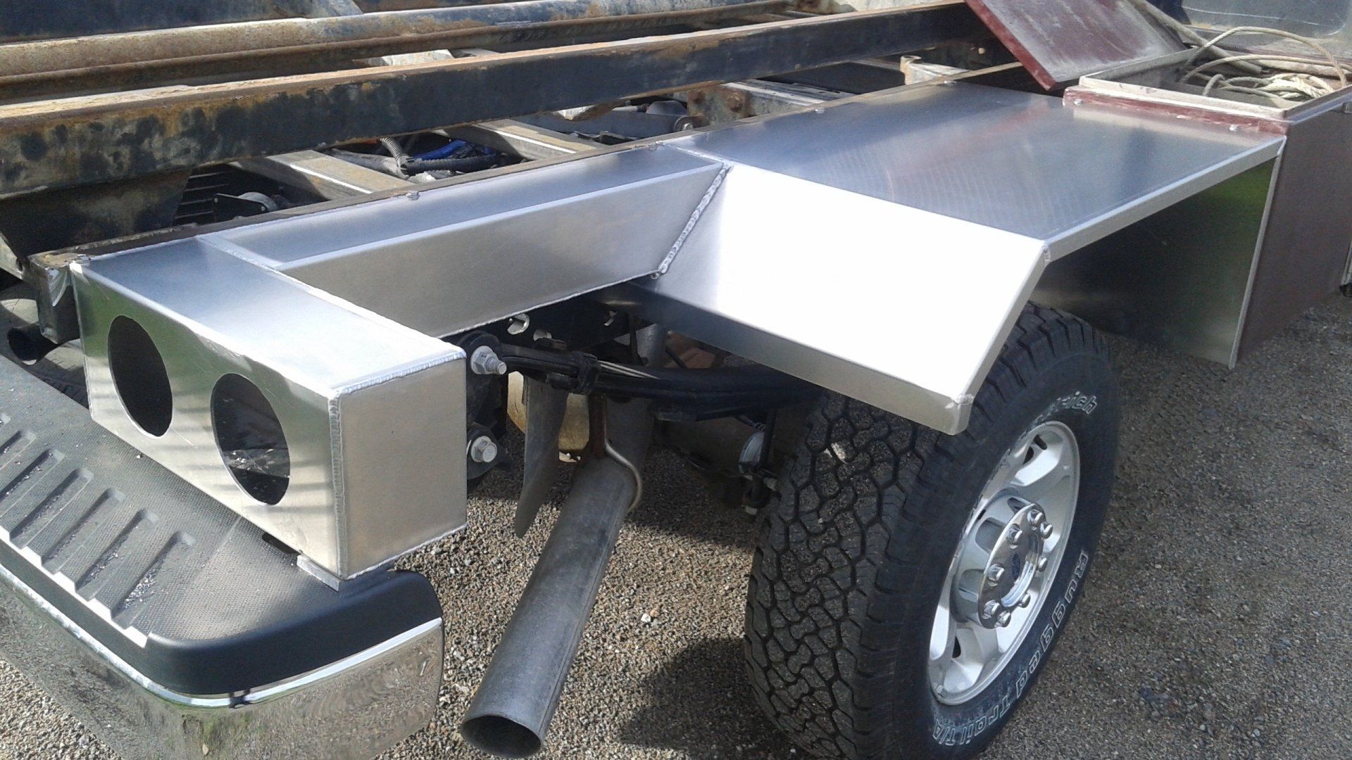 Un camion avec une aile en acier inoxydable est garé sur une route de gravier