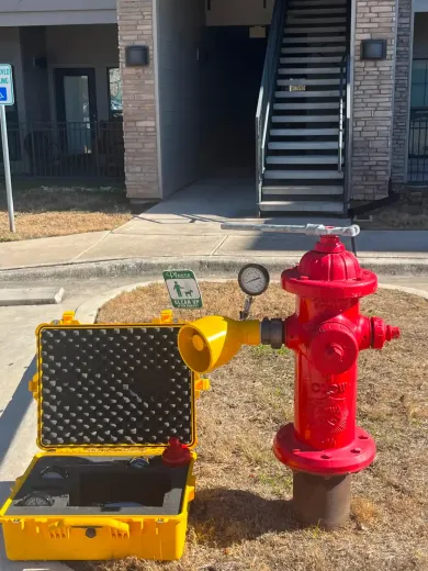 Red fire hydrant with yellow testing equipment, near a building with stairs, a handicap parking sign, and grass.