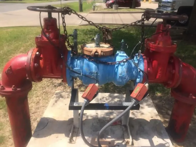 Red and blue pipes with valves secured by chains and a lock, outdoors.