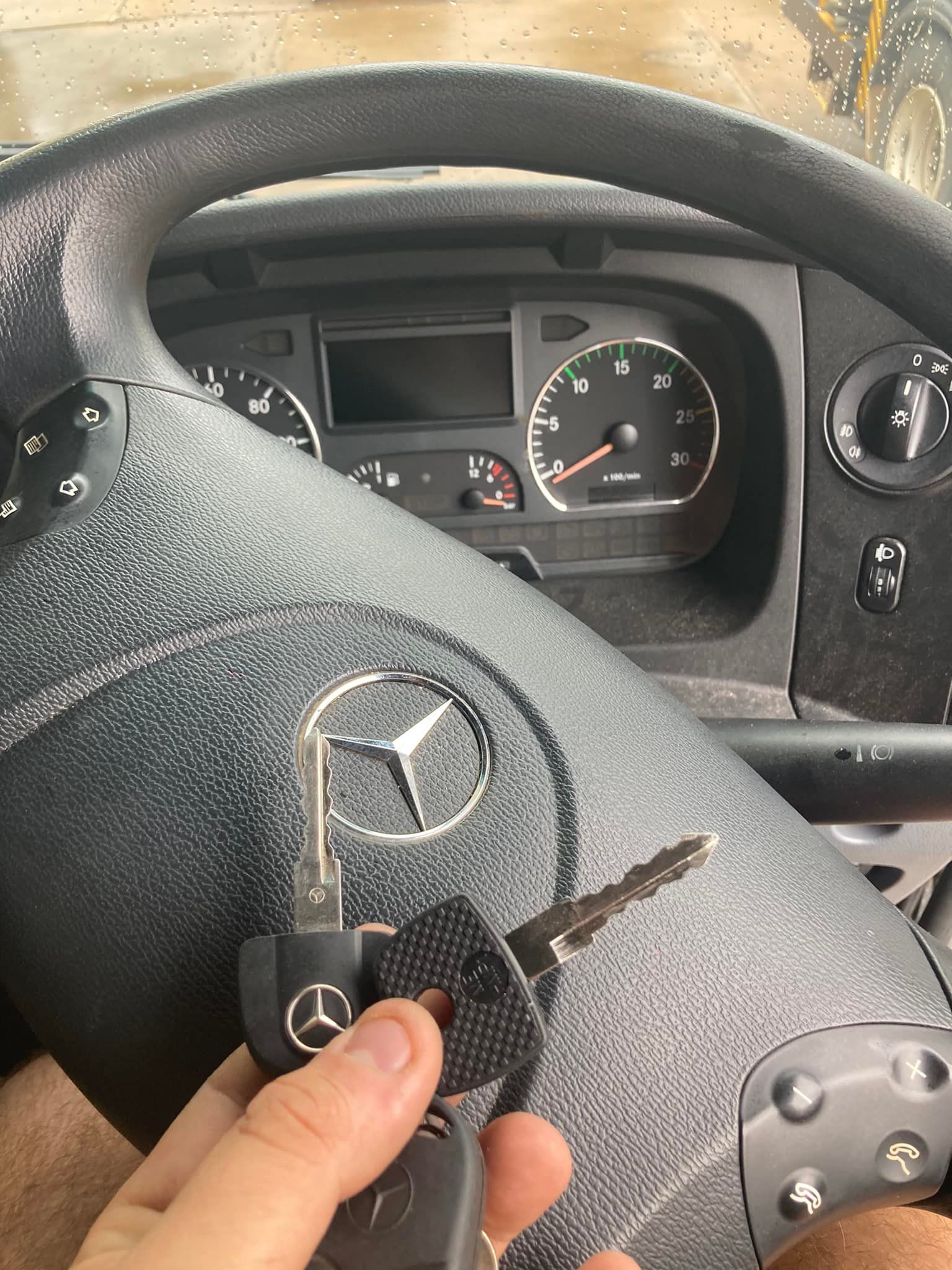 Hand holding Mercedes-Benz keys in a truck cab, steering wheel in front of dashboard and gauges.— Locksmiths In Thuringowa Central, QLD