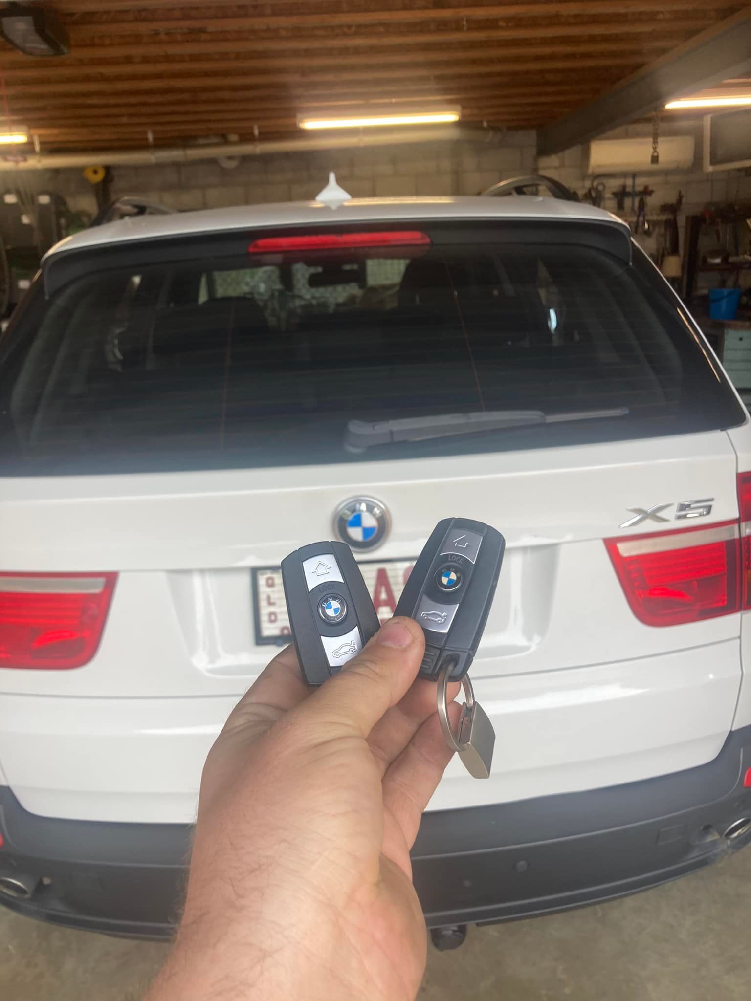 Person holding two BMW car keys in front of a white BMW X5 SUV.— Locksmiths In Thuringowa Central, QLD