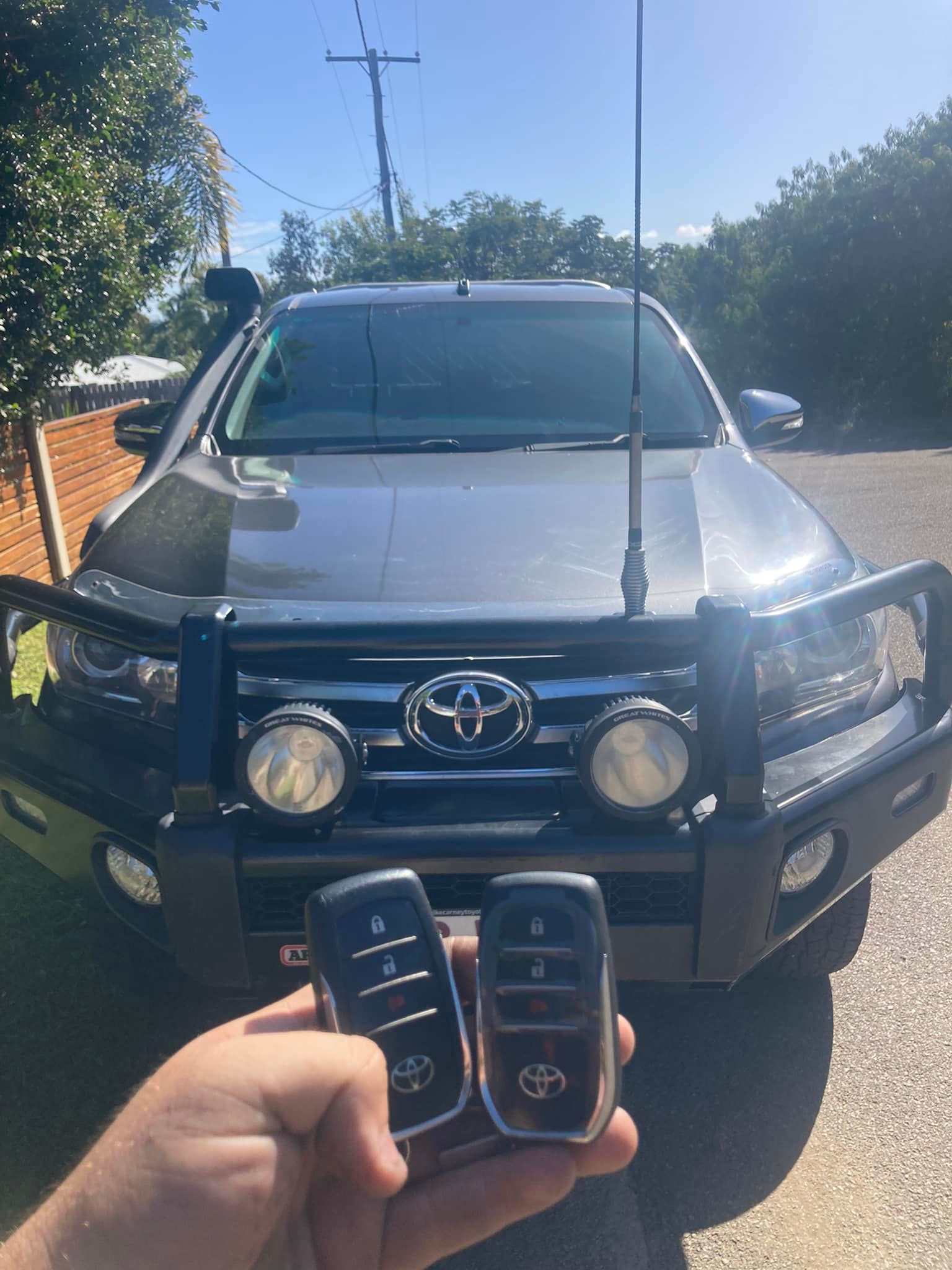 Person holding two car keys in front of a dark Toyota truck with bull bar, antenna, and spotlights.— Locksmiths In Thuringowa Central, QLD