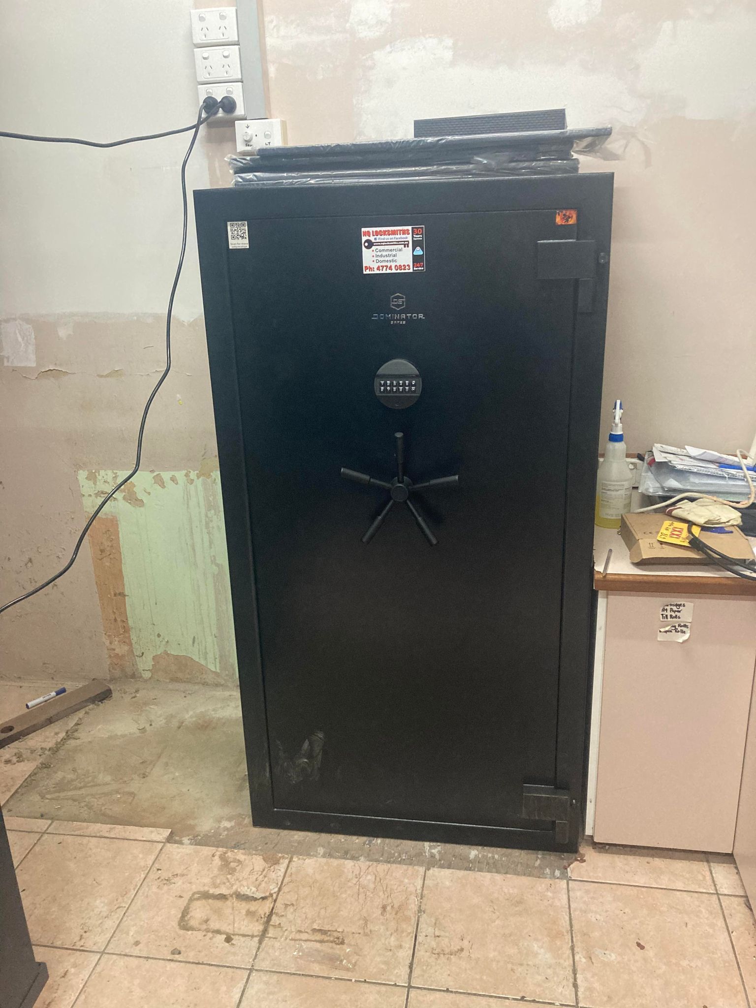 Large black safe with a star-shaped handle, in a room with exposed wall and a countertop.— Locksmiths In Thuringowa Central, QLD