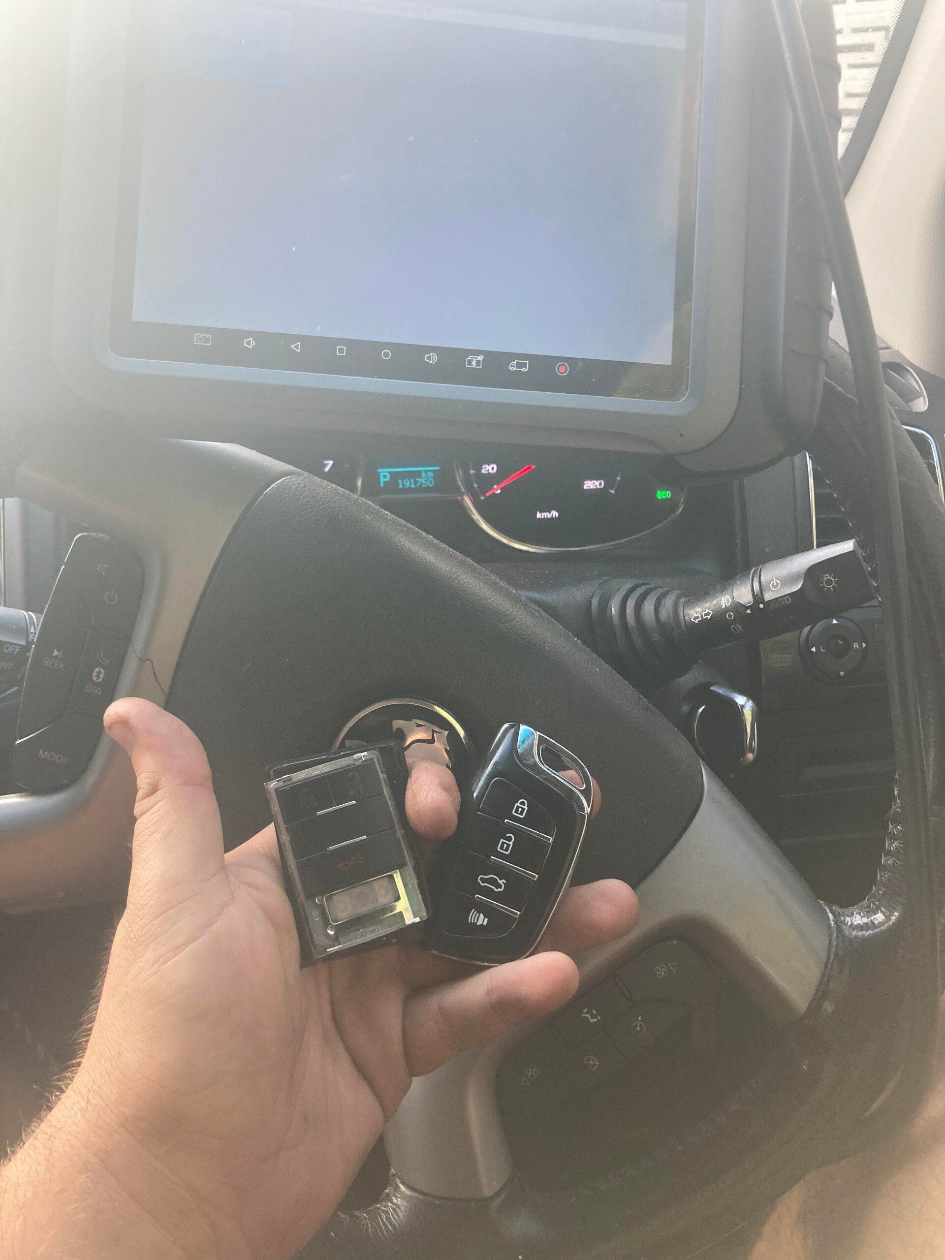 A person holding two car key fobs inside a vehicle, near a steering wheel and dashboard.— Locksmiths In Thuringowa Central, QLD