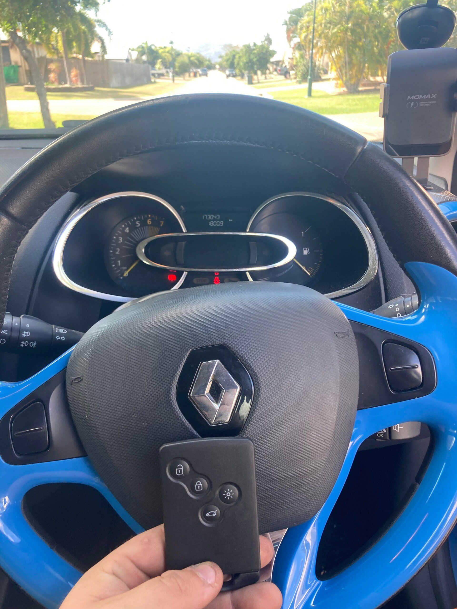 A person holding a Renault car key inside a blue and black steering wheel; dashboard visible.— Locksmiths In Thuringowa Central, QLD